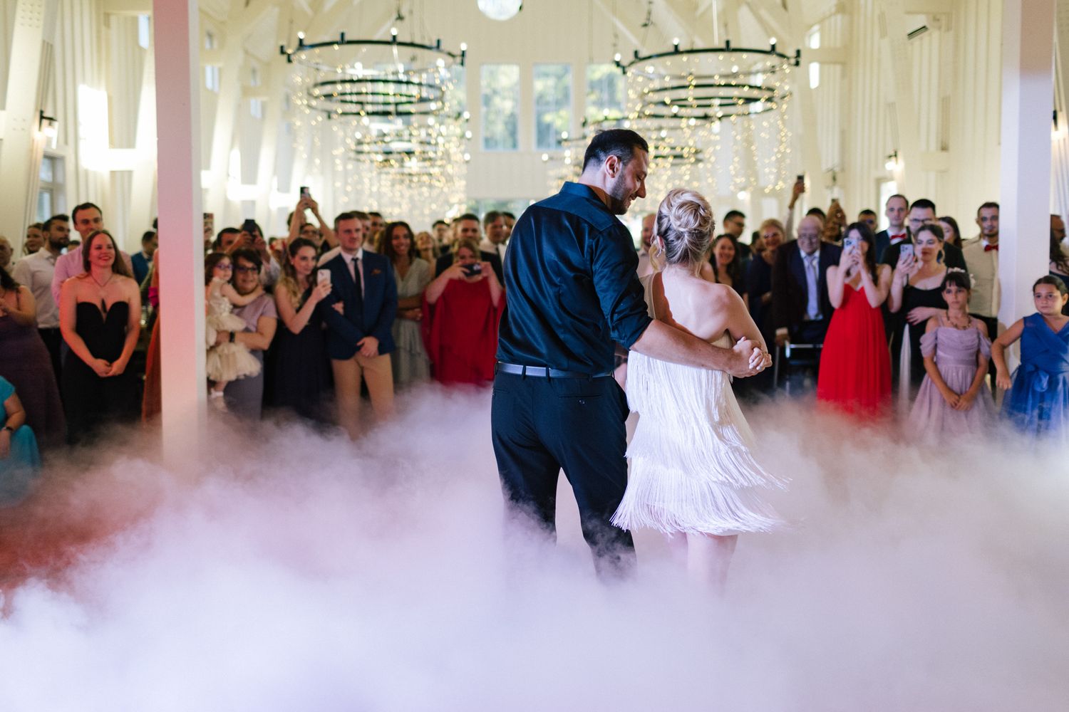 Couples dancing in a bright reception hall with dramatic lighting effects.