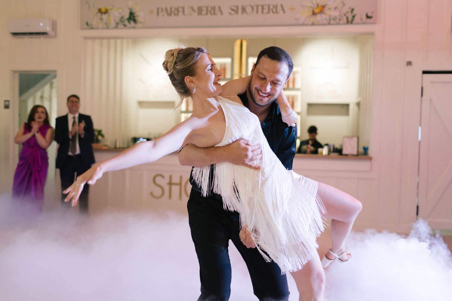 A couple performs an energetic dance lift during their wedding celebration with fog effects.