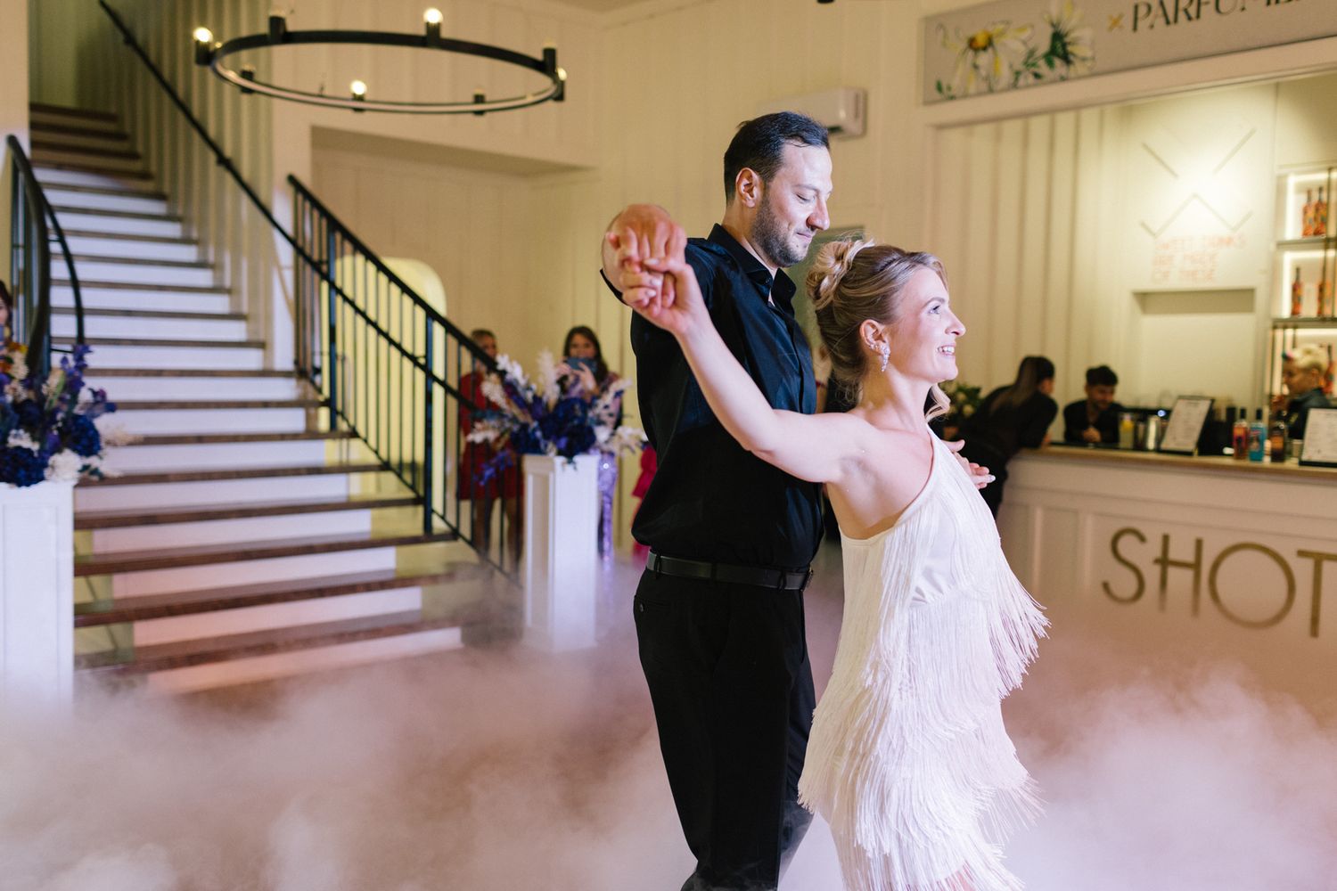 A couple performs an elegant dance move in a venue with stairs and fog effects.