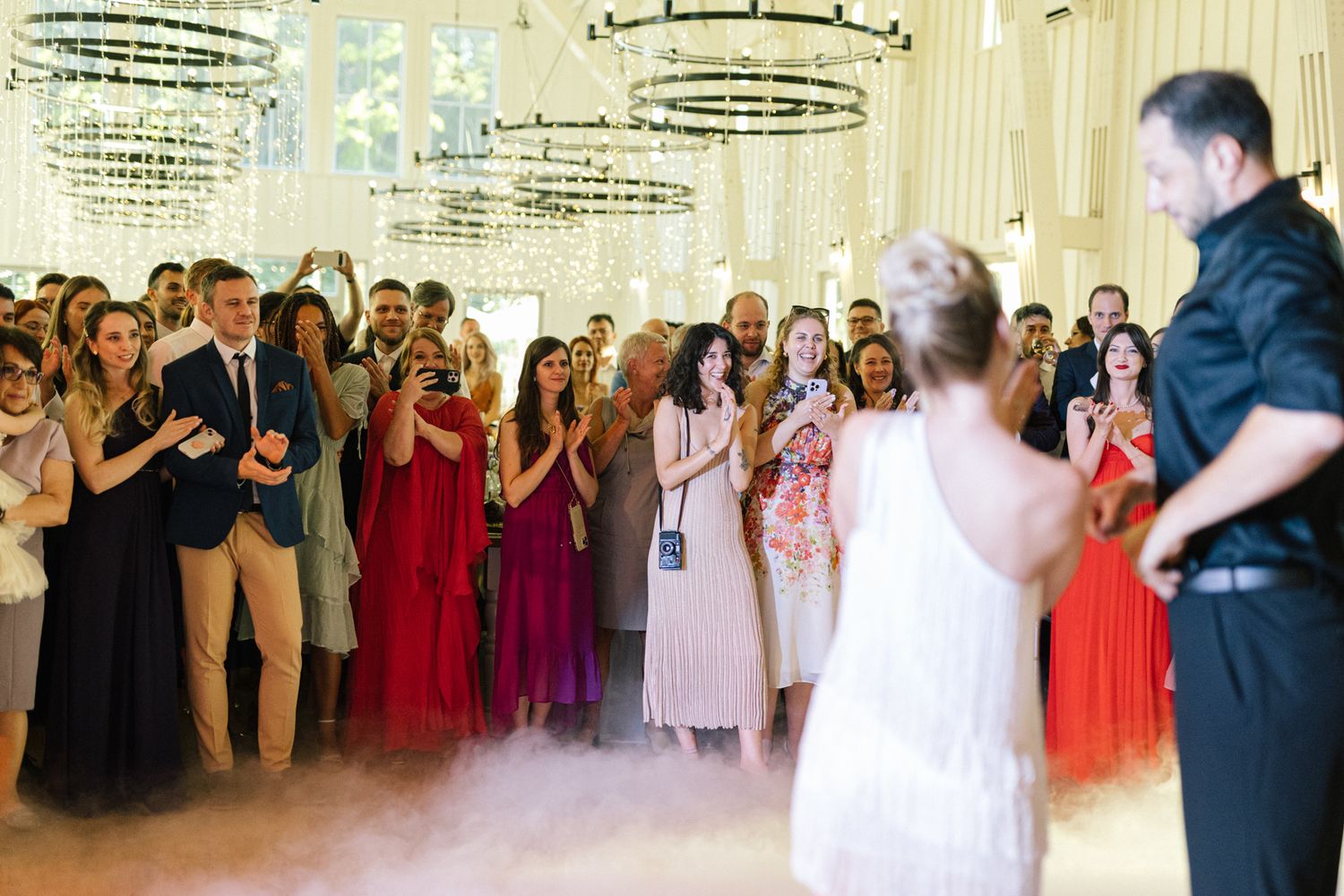 Guests gather around a dance floor as a couple performs their first dance under crystal chandeliers.