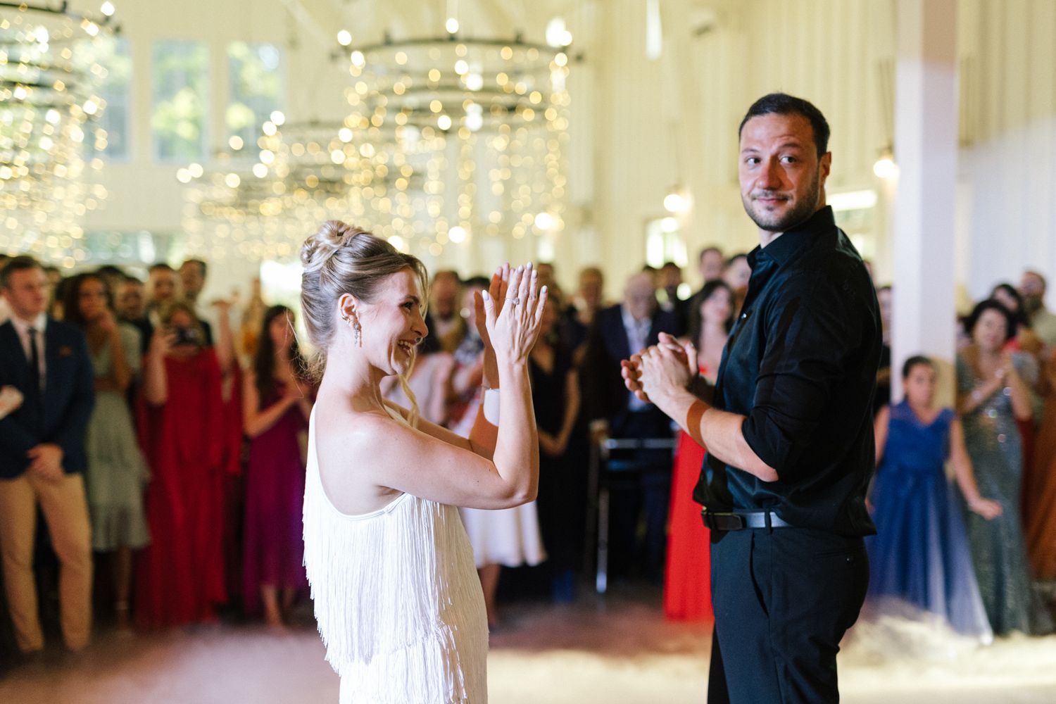 Wedding celebration in an elegant ballroom with guests watching dancers under sparkling chandeliers.