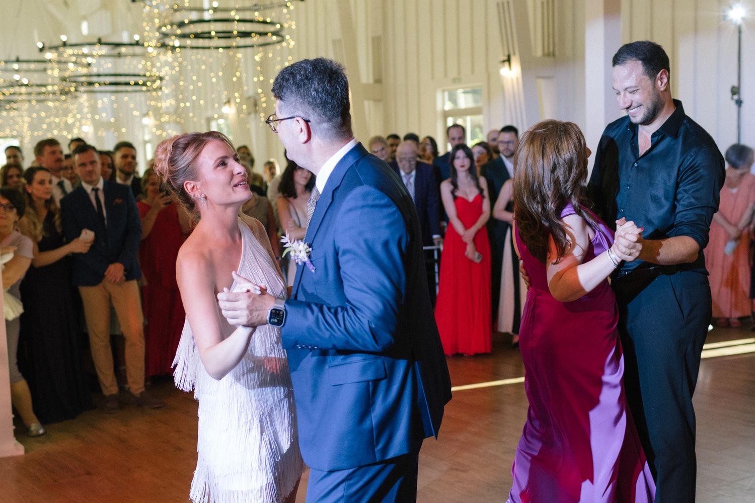 Wedding guests dance and celebrate in a beautifully decorated ballroom with hanging chandeliers.