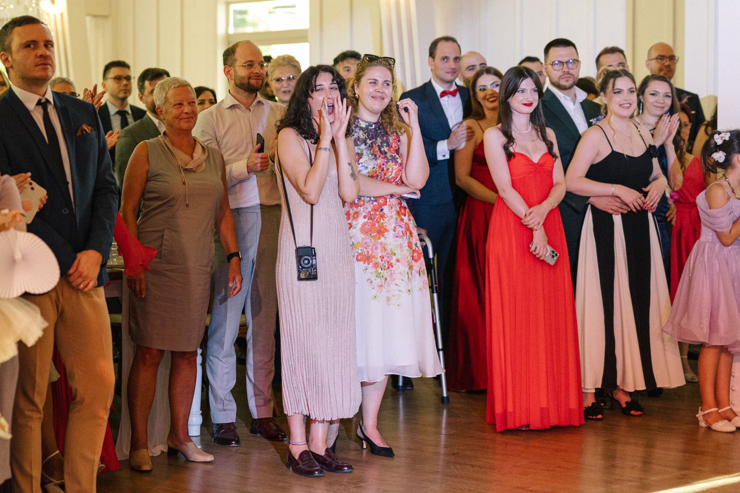 Wedding reception guests line the dance floor watching celebrations in an elegant venue with chandeliers.