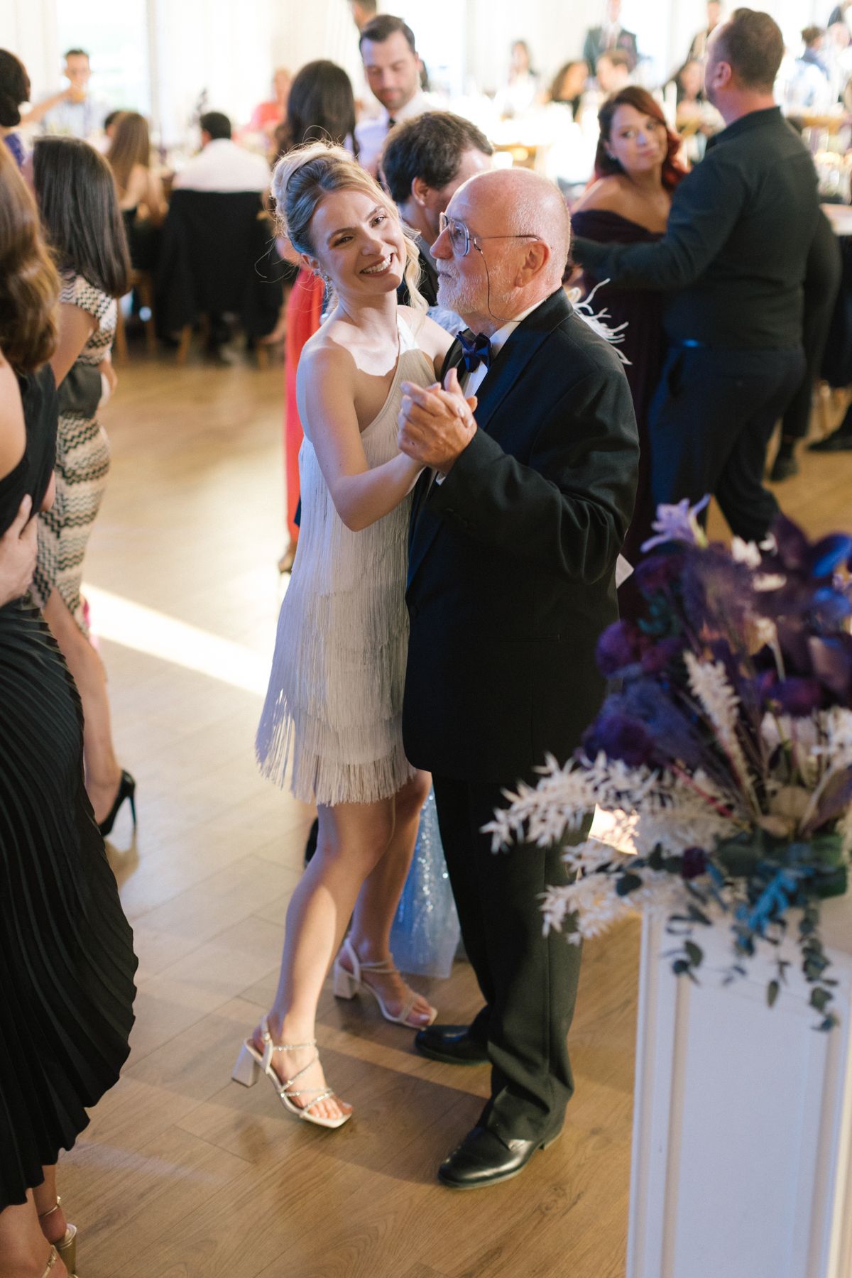Wedding guests dancing on an elegant dance floor decorated with purple floral arrangements.
