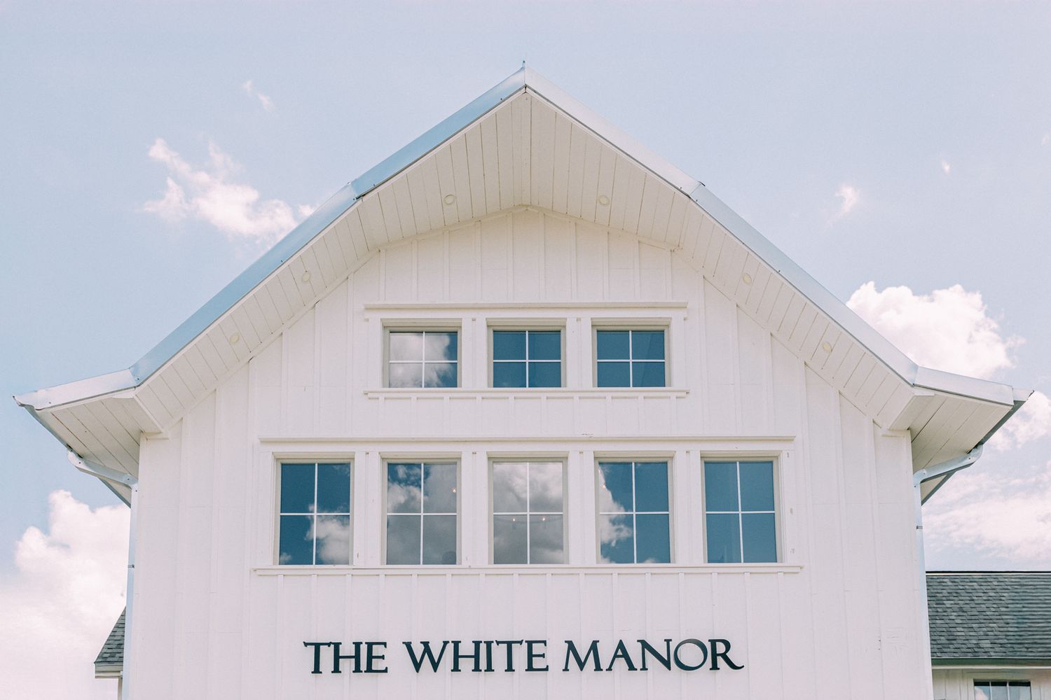 White manor house exterior with classic architectural details against blue sky.