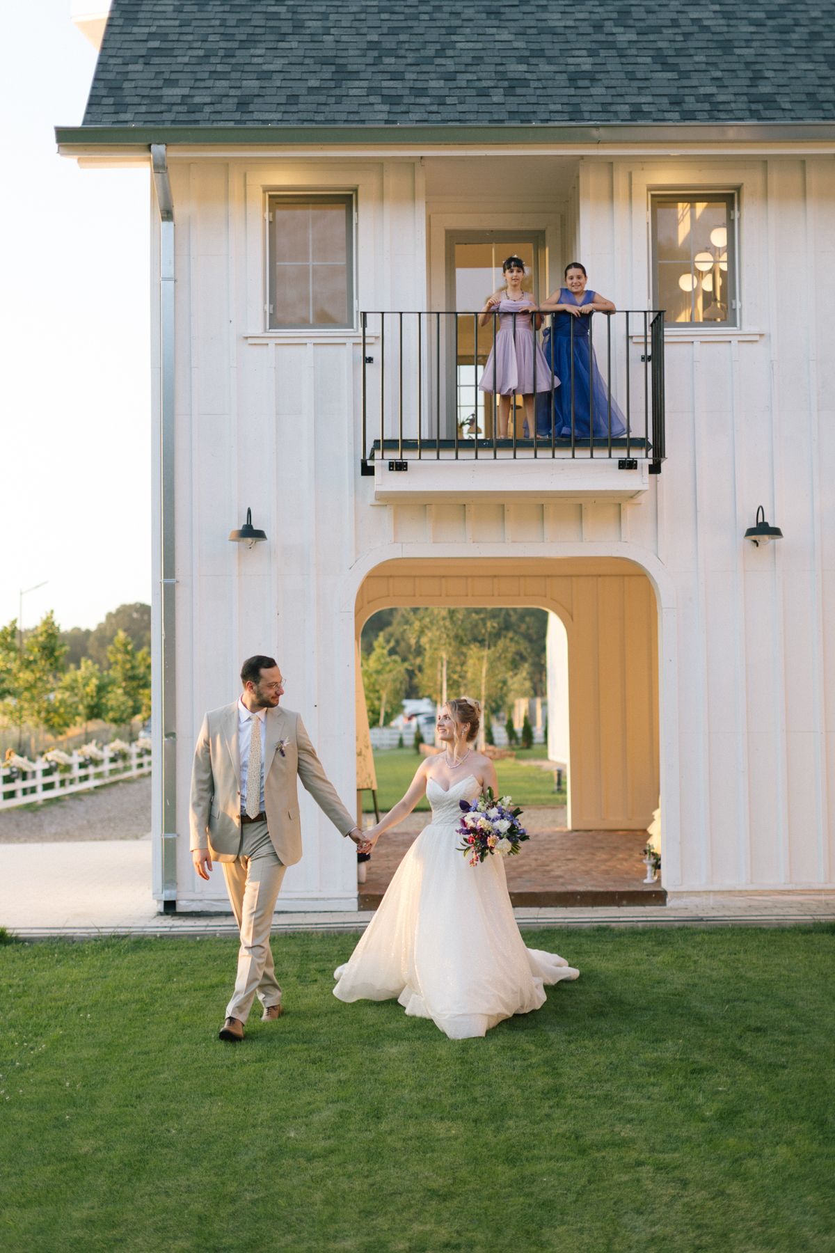 Couple dancing playfully outside a white building with balcony and arched doorway.