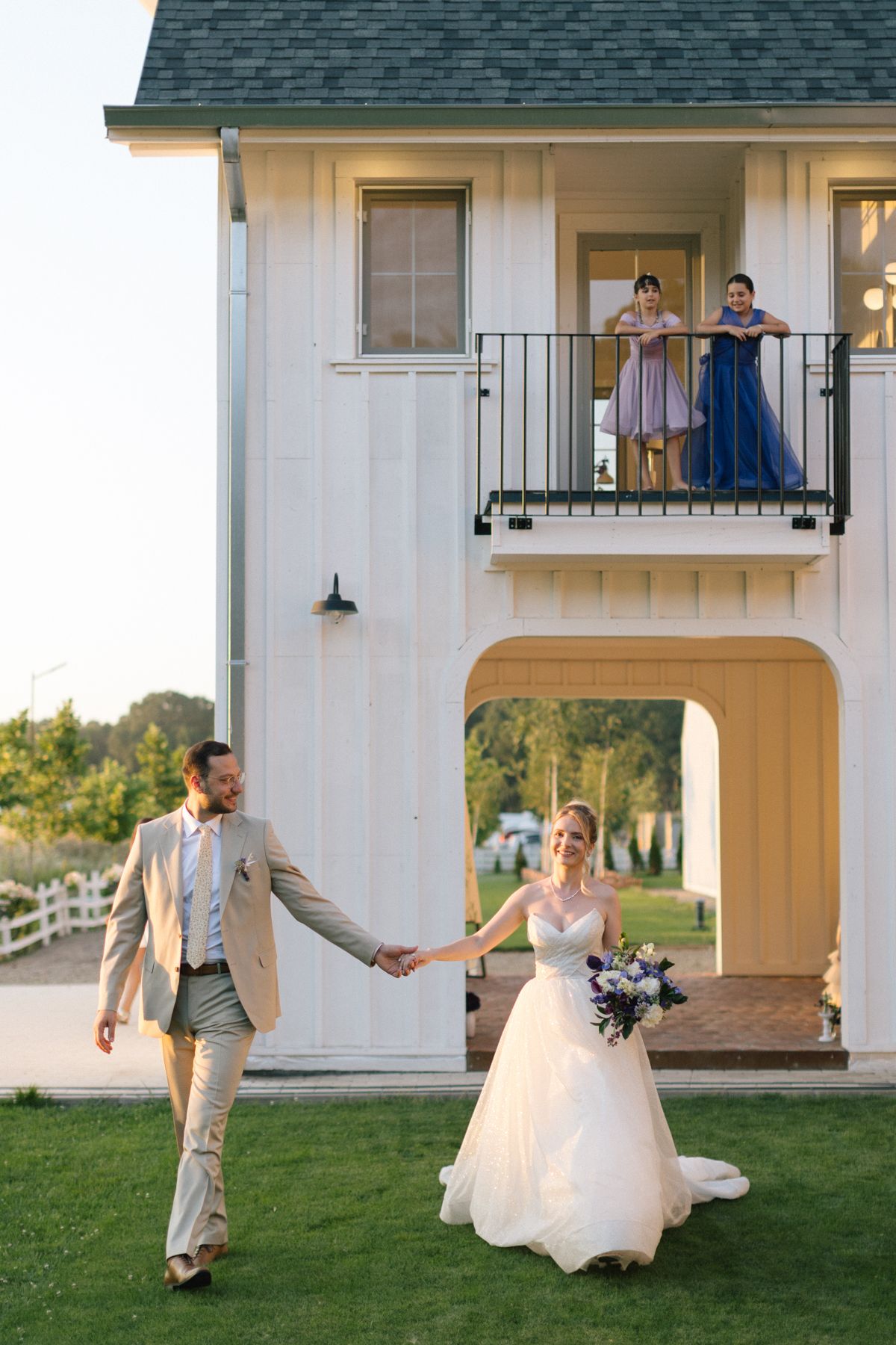 Wedding couple dancing and twirling on lawn in front of white building.