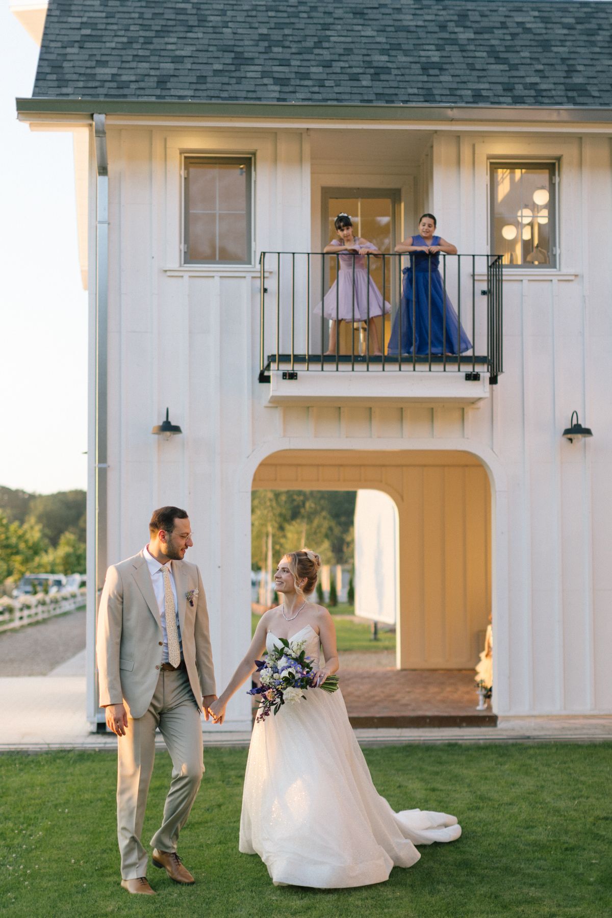 Bride and groom dancing together on grass in front of white farmhouse style venue.
