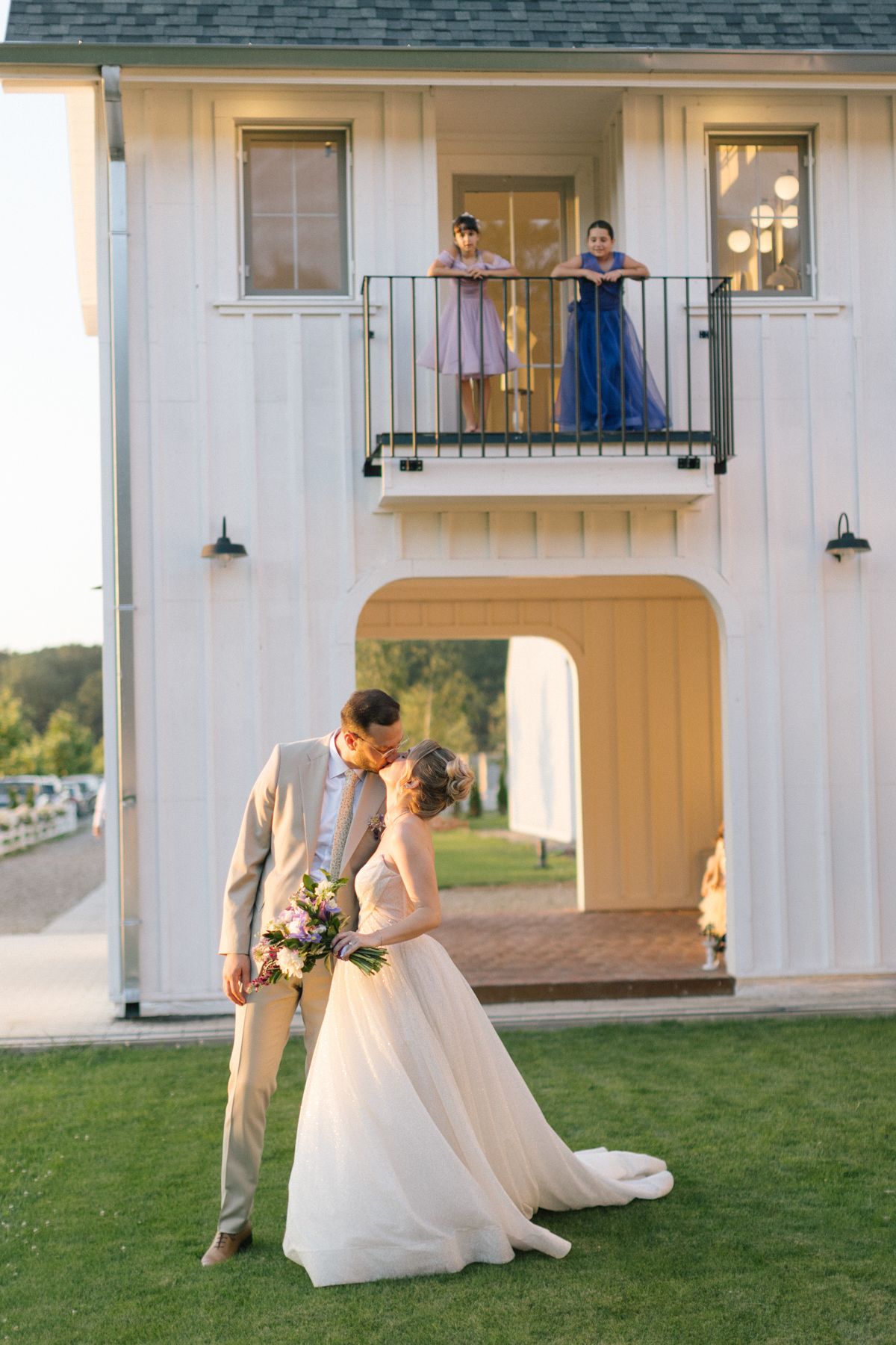 A couple shares a romantic moment in front of a white barn building during their wedding photoshoot.