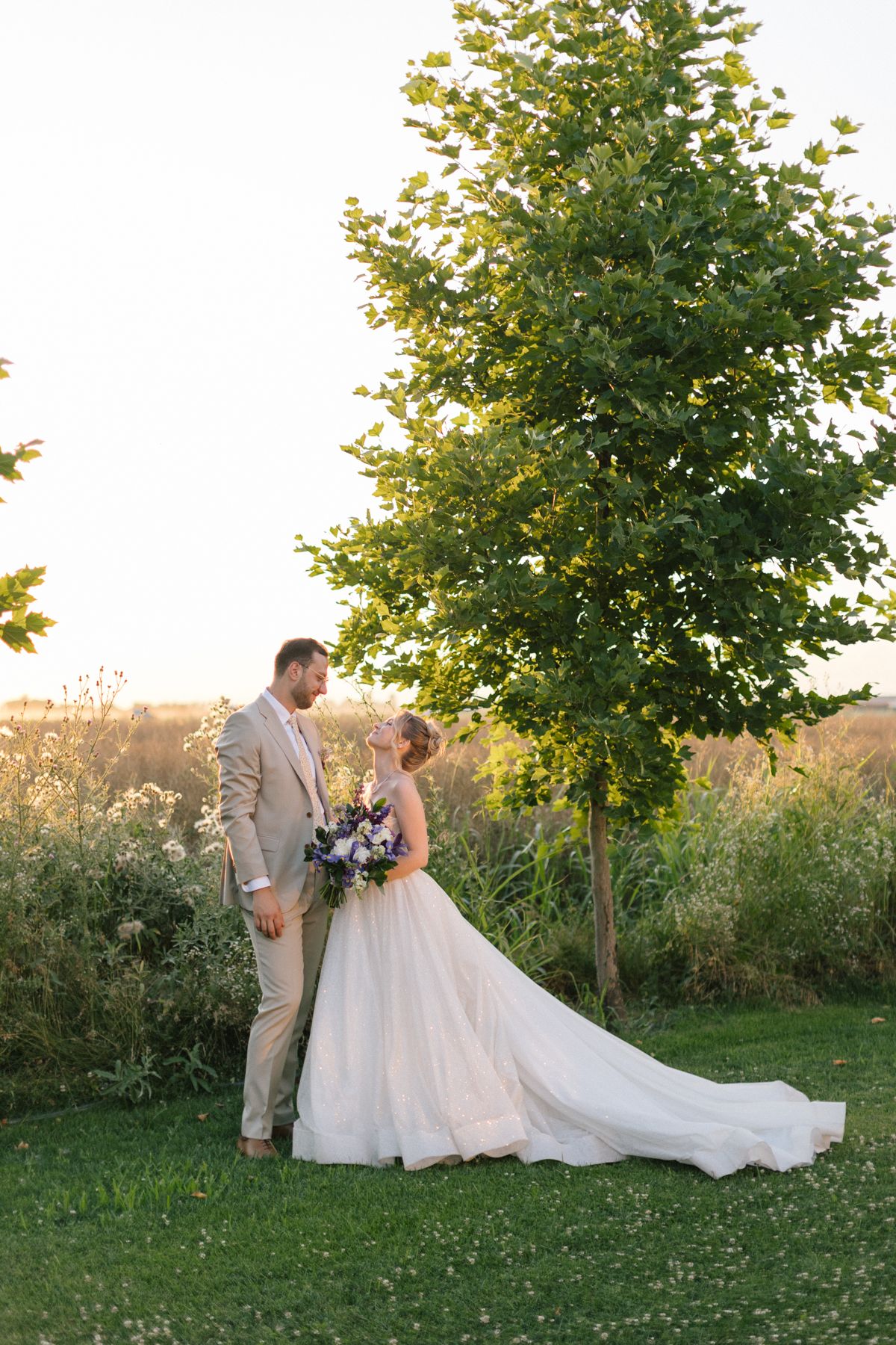 Newlyweds share intimate moments against a backdrop of trees during golden hour.