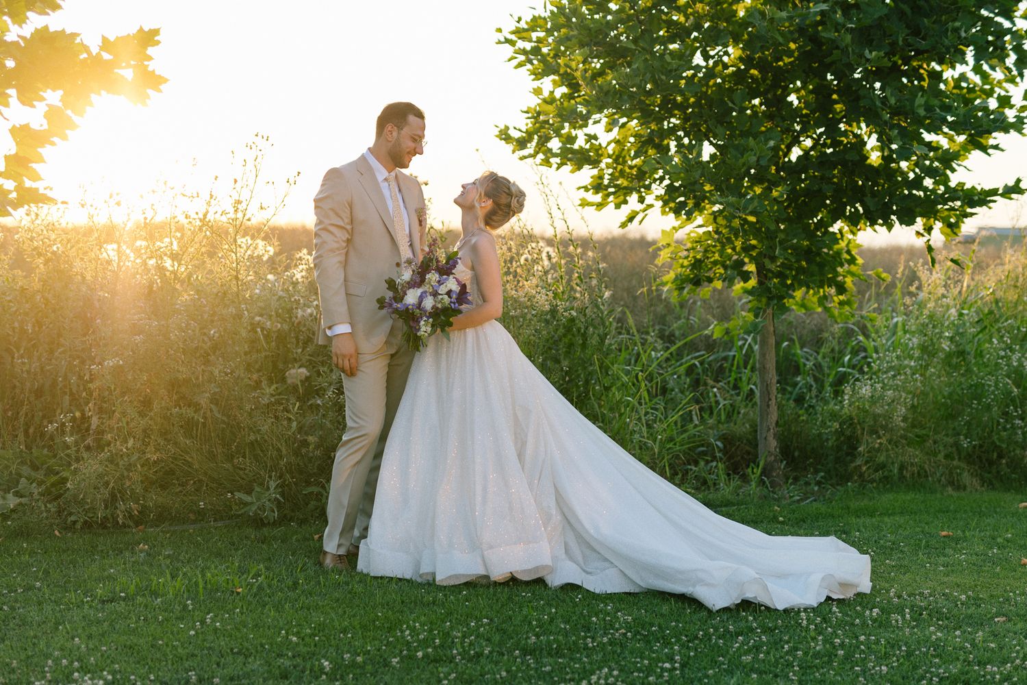 Wedding couple embraces in a sun-drenched garden setting with flowing white dress.
