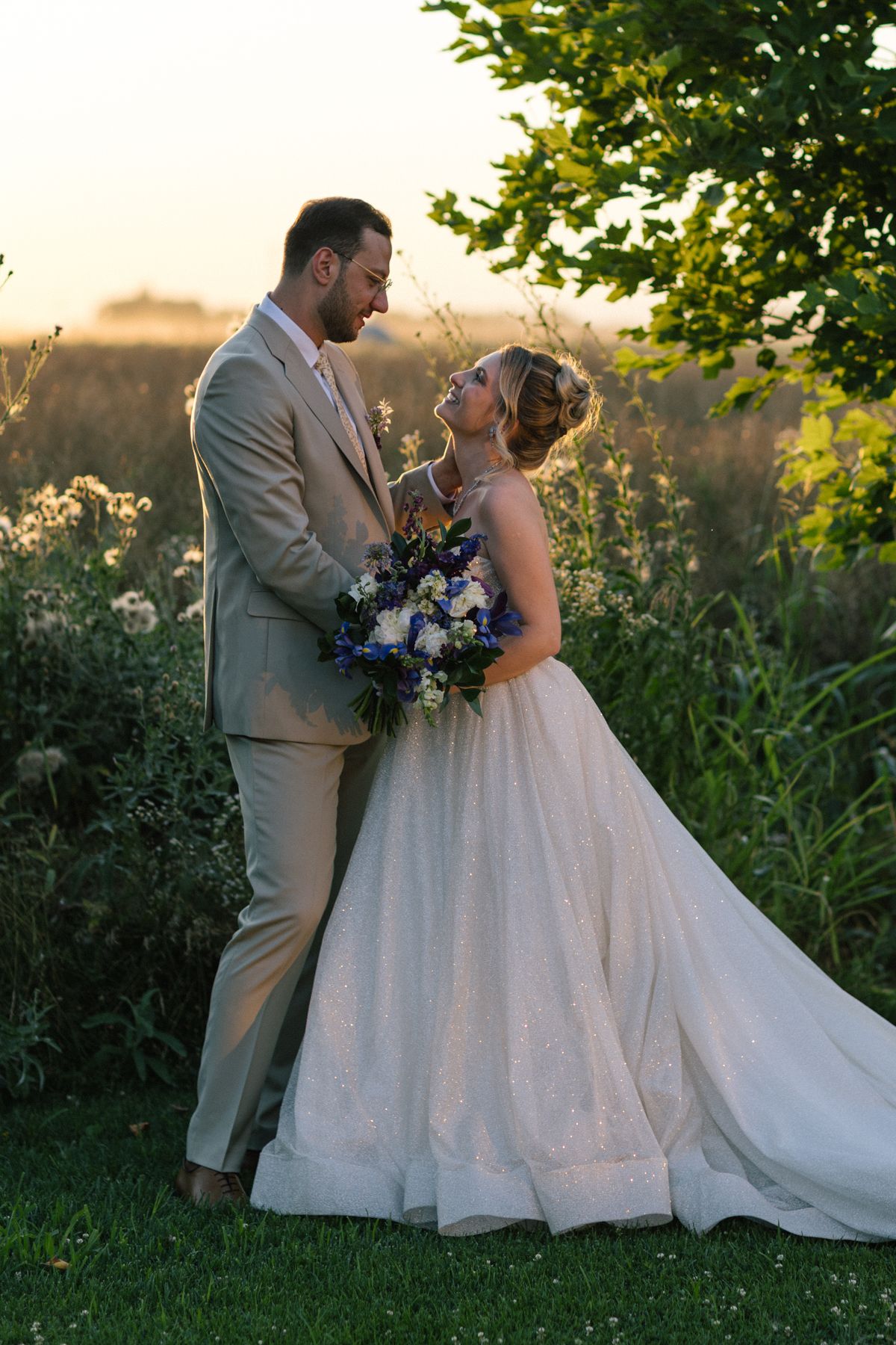 Elegant wedding couple poses together on manicured lawn with natural backdrop.