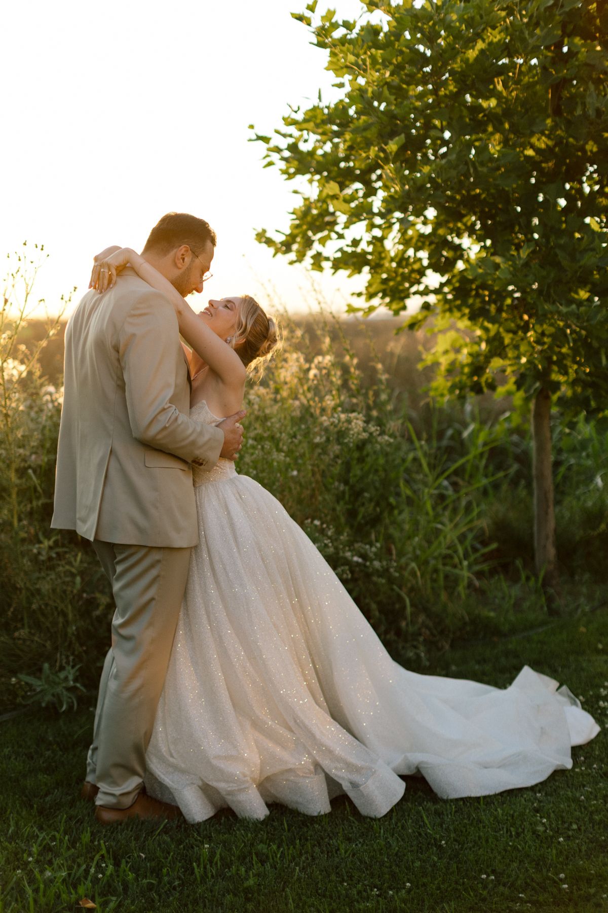 Newlyweds share a romantic dip pose in a lush outdoor garden setting.