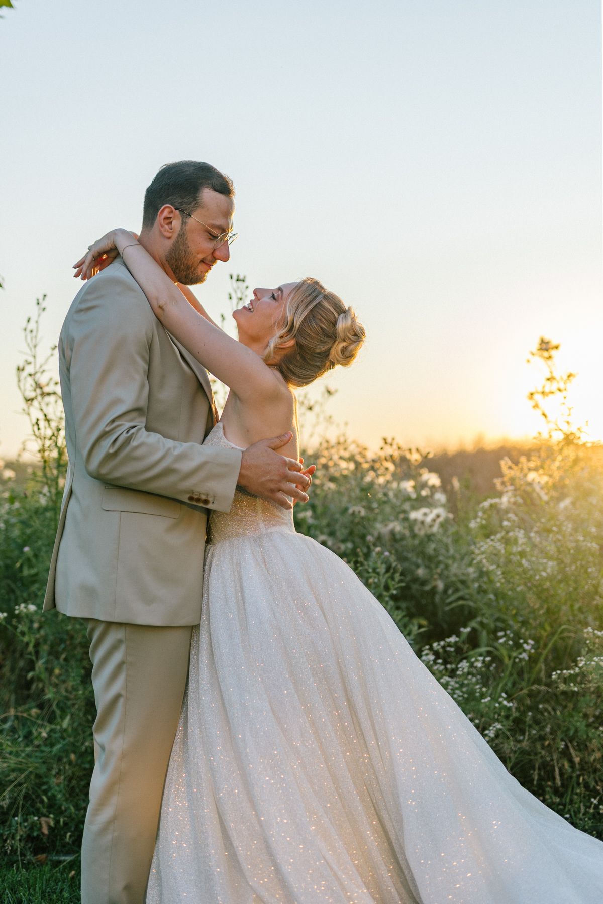 A wedding couple shares an intimate moment at sunset in a wildflower field.