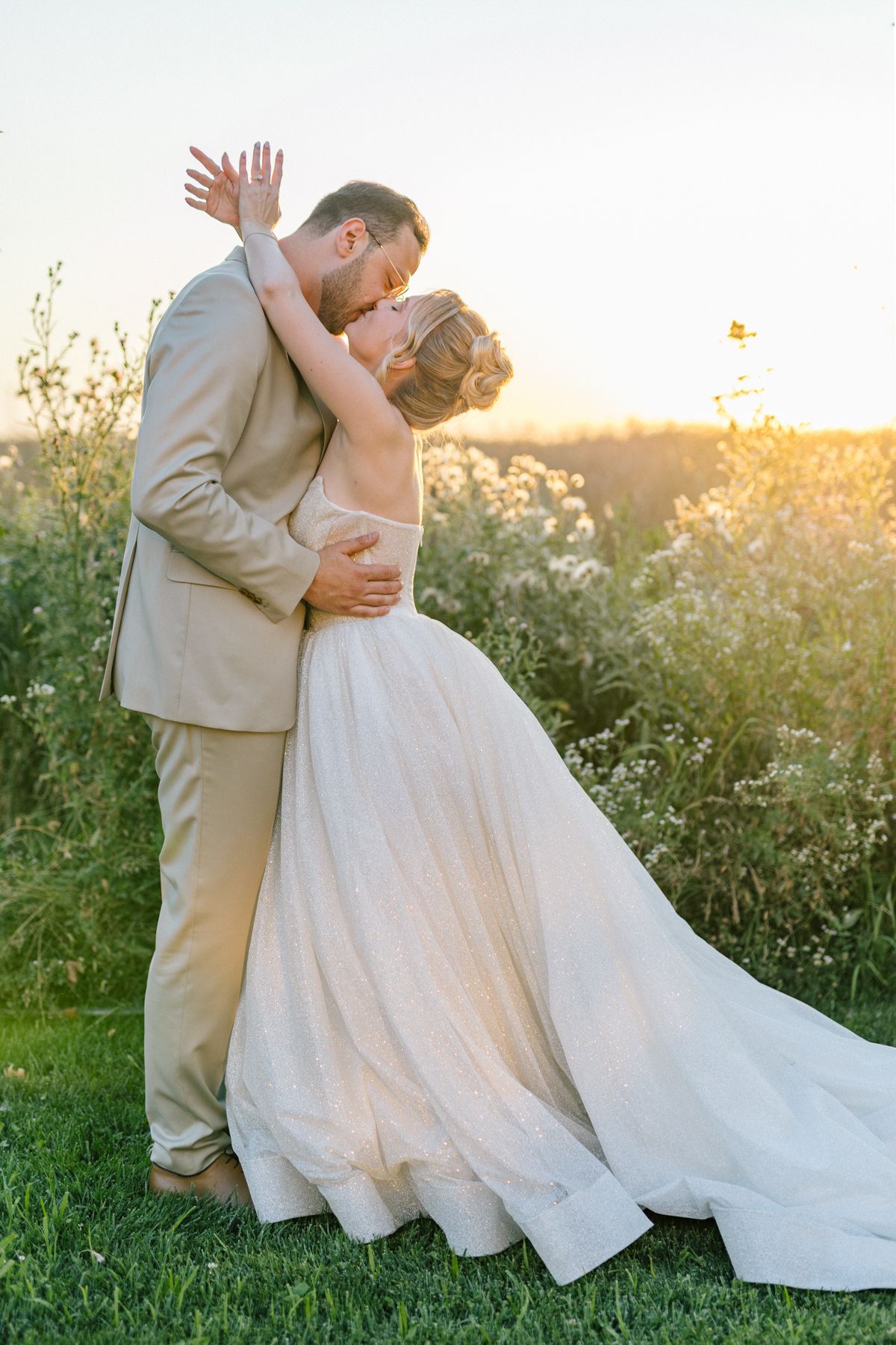 A romantic wedding pose captured in a meadow during golden hour.