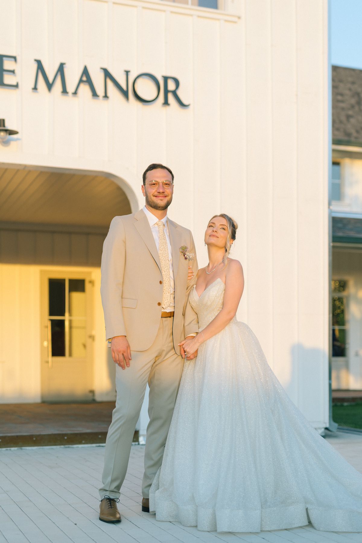 Newlyweds share a romantic moment outside The Manor venue in elegant wedding attire.