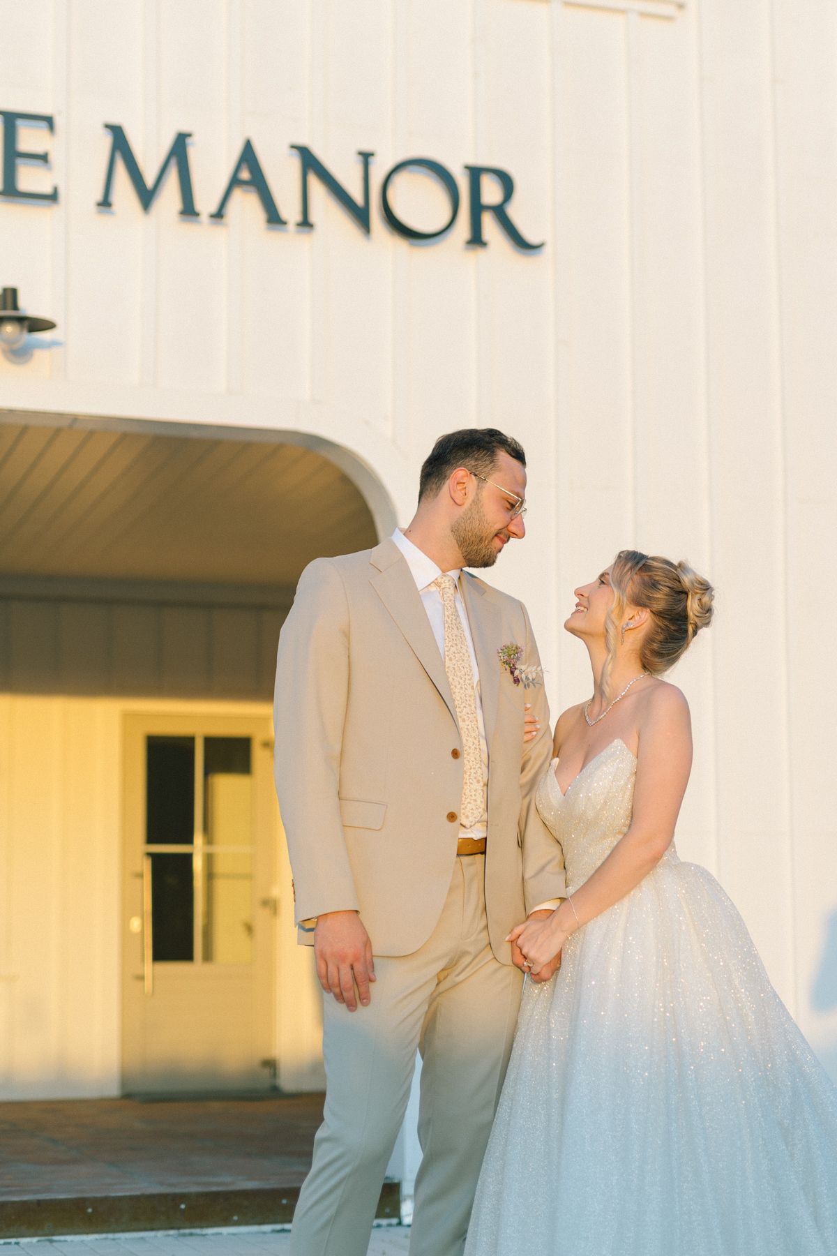 Bride in ballgown and groom in tan suit share candid moment at The Manor.