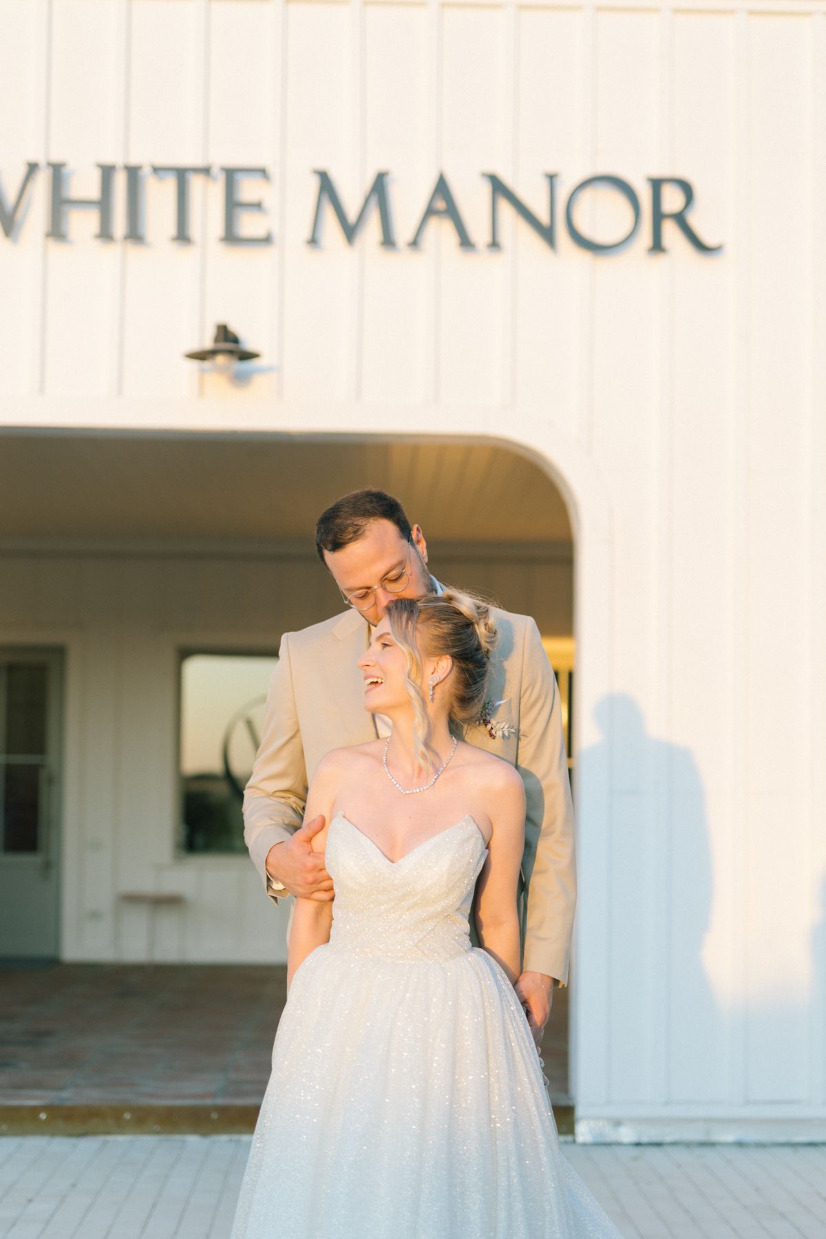 Joyful wedding couple shares intimate moment against white building exterior.
