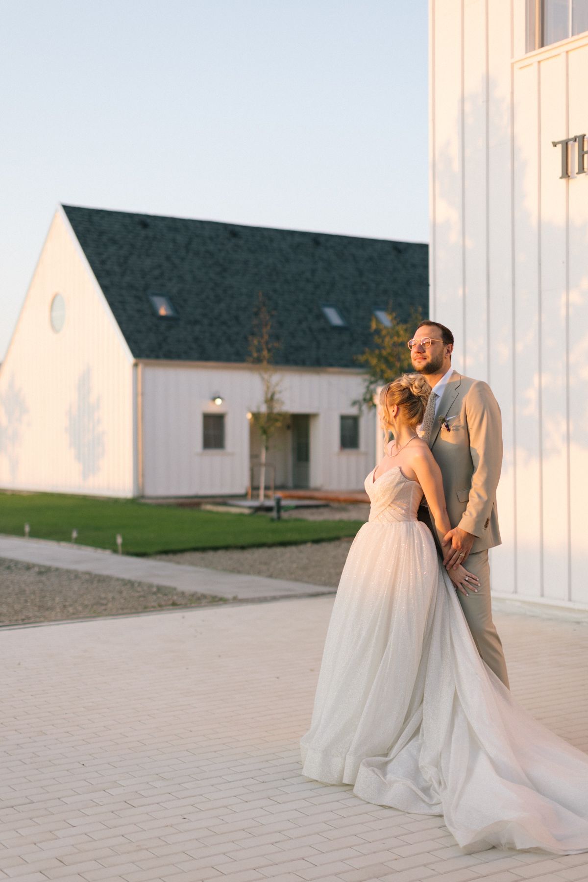 Wedding couple poses for romantic portraits outside white barn venue.