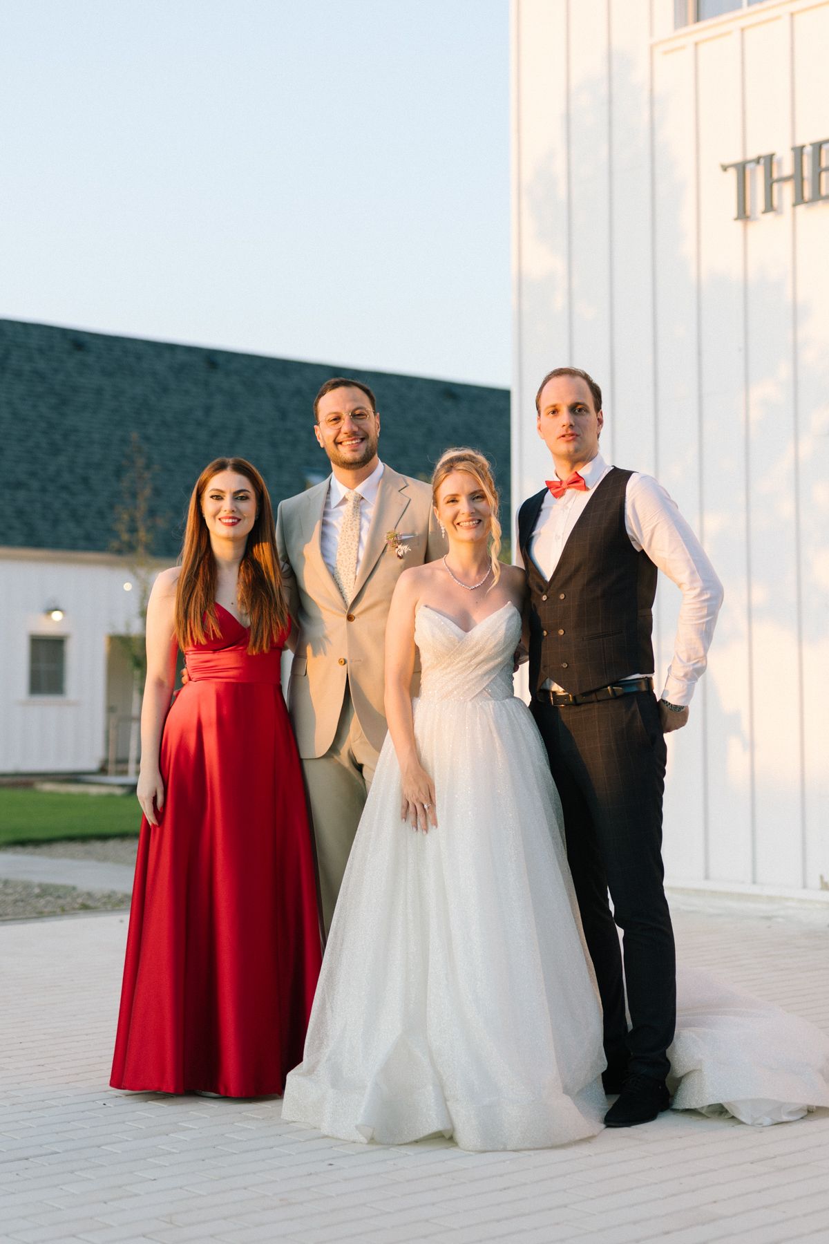 Wedding party in red and white attire poses outside The White Manor.