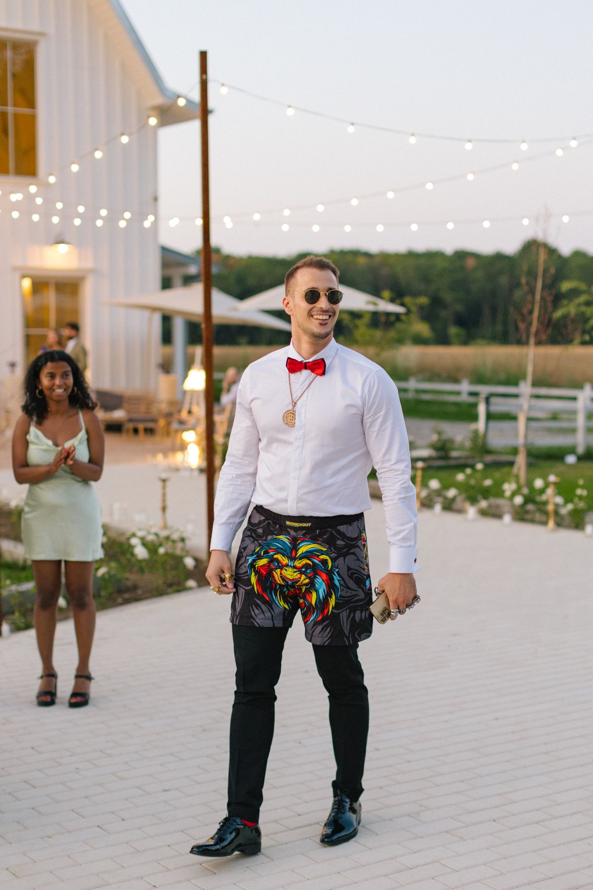 Wedding guest dances on outdoor patio wearing colorful pants and red bowtie.