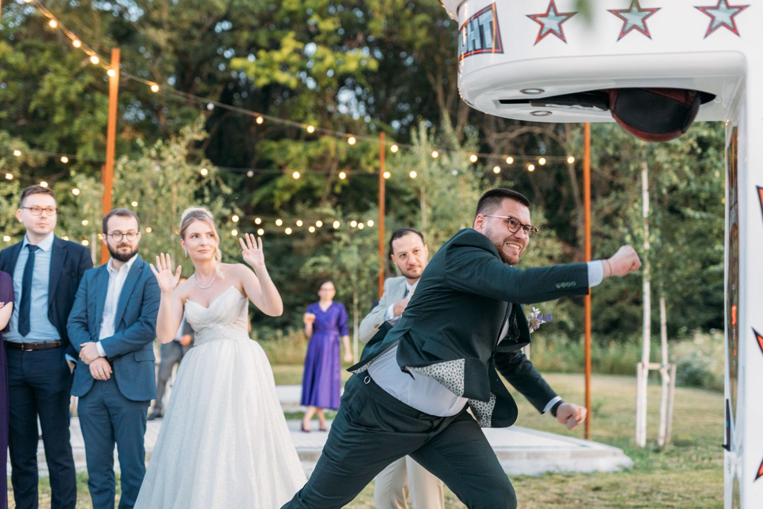 Wedding party members take turns playing a carnival-style punching game at an outdoor venue.