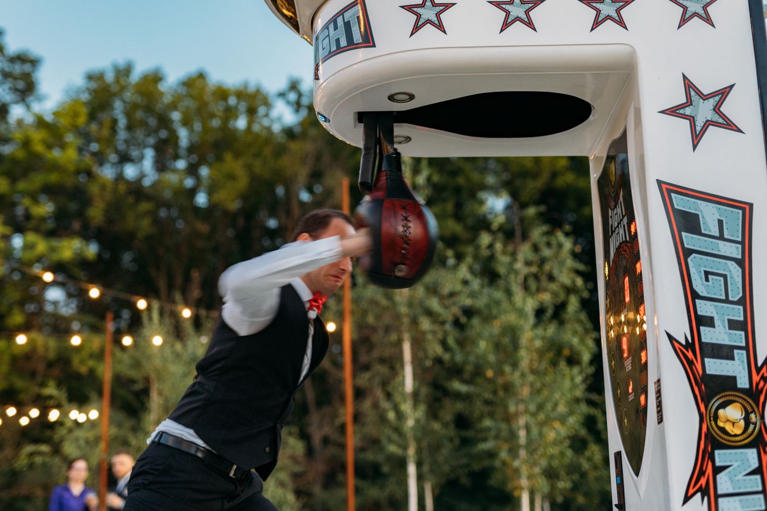 Guests compete at a carnival-style punching game machine decorated with stars during an evening wedding reception.