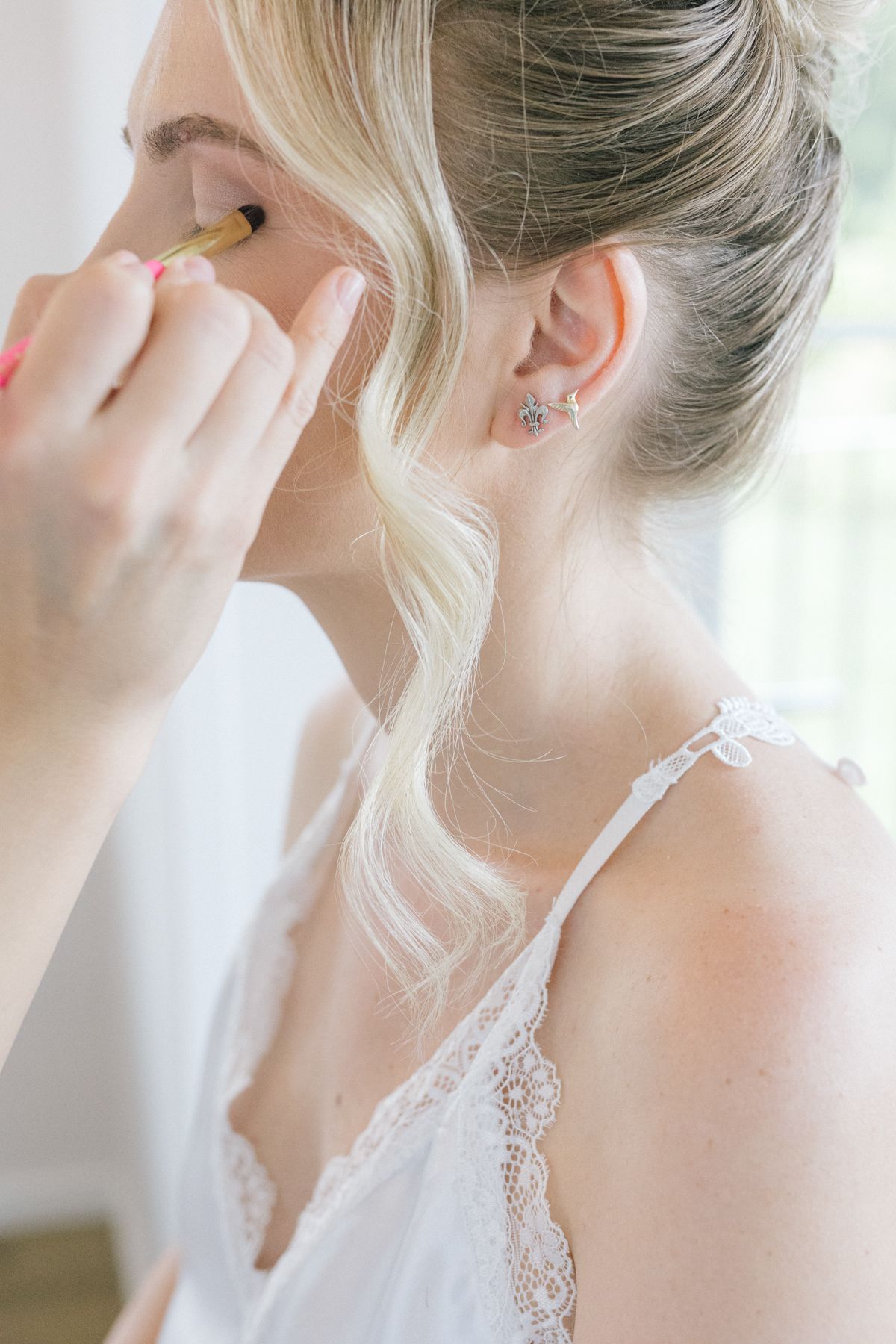 Close-up of delicate pearl earrings being put on against a light background.