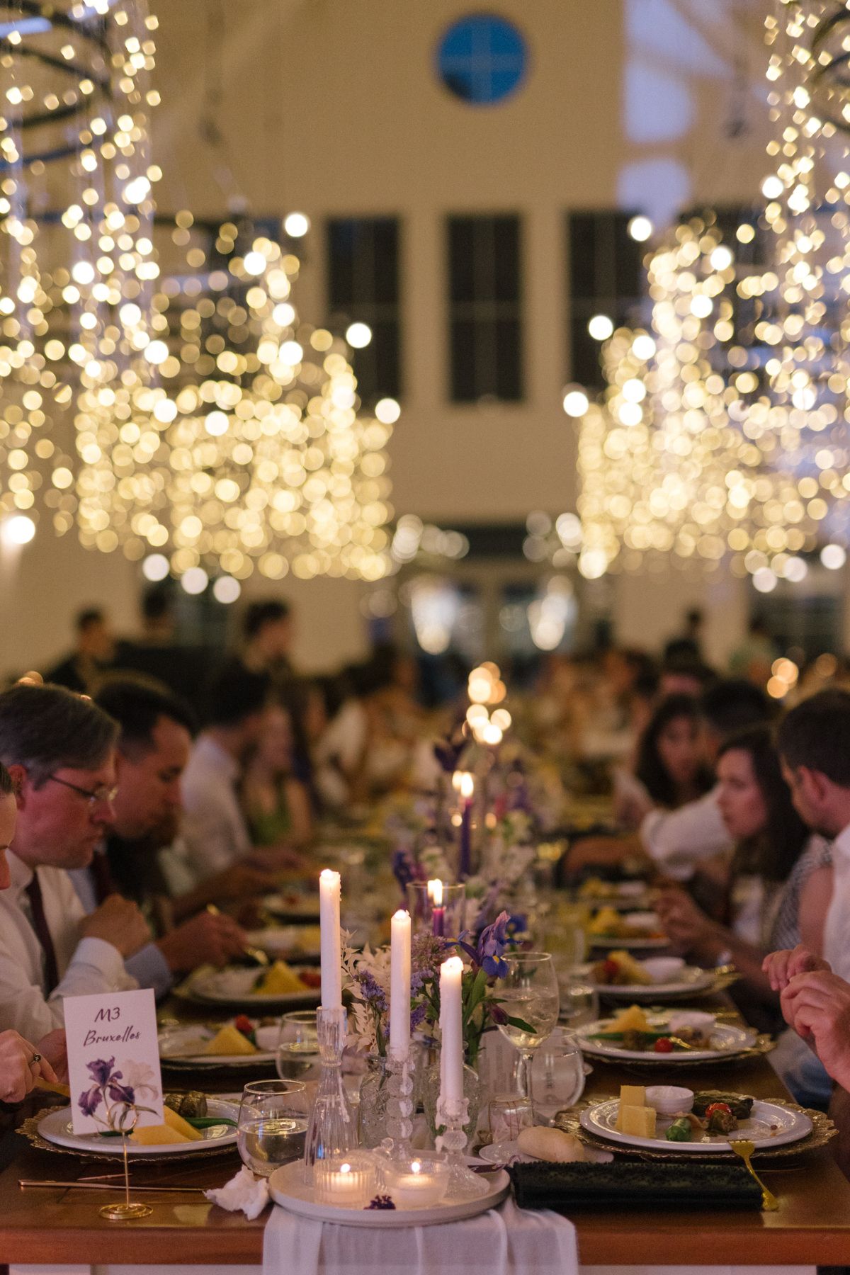 Wedding reception tables decorated with candles and place settings under cascading string lights.