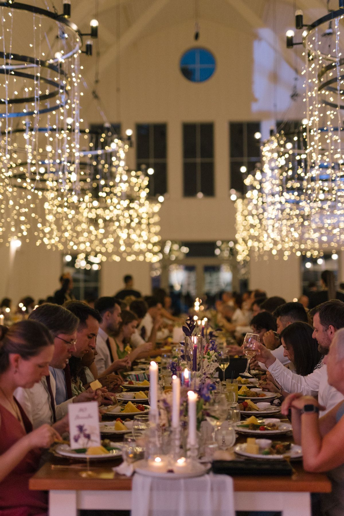 Long banquet tables under twinkling fairy lights with guests seated for a formal dinner.