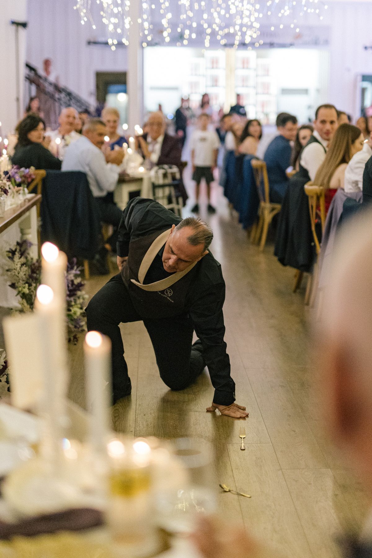 Guest showing off dance moves at wedding reception under string lights.
