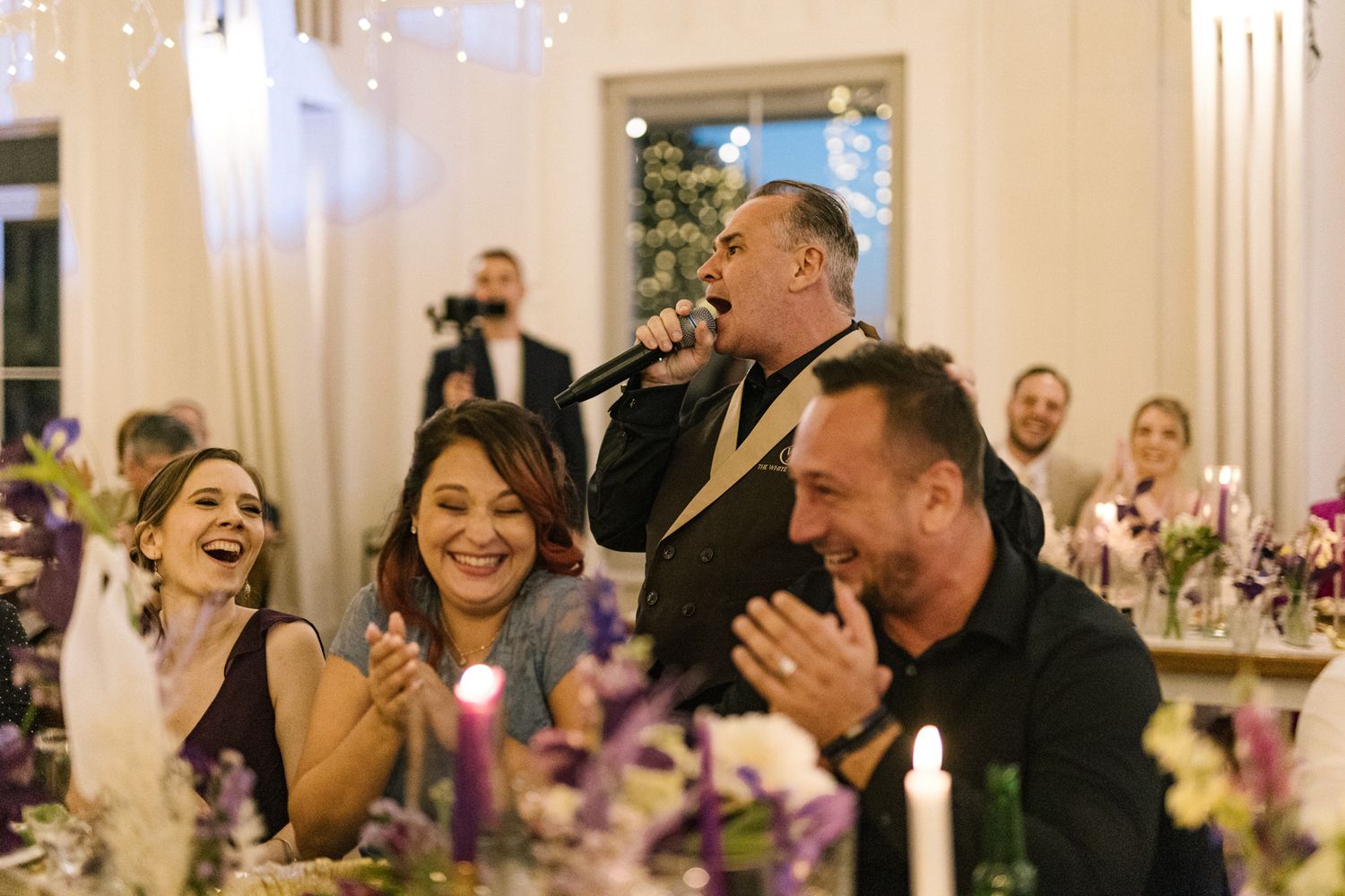 Joyful wedding guests laughing and clapping during reception dinner.