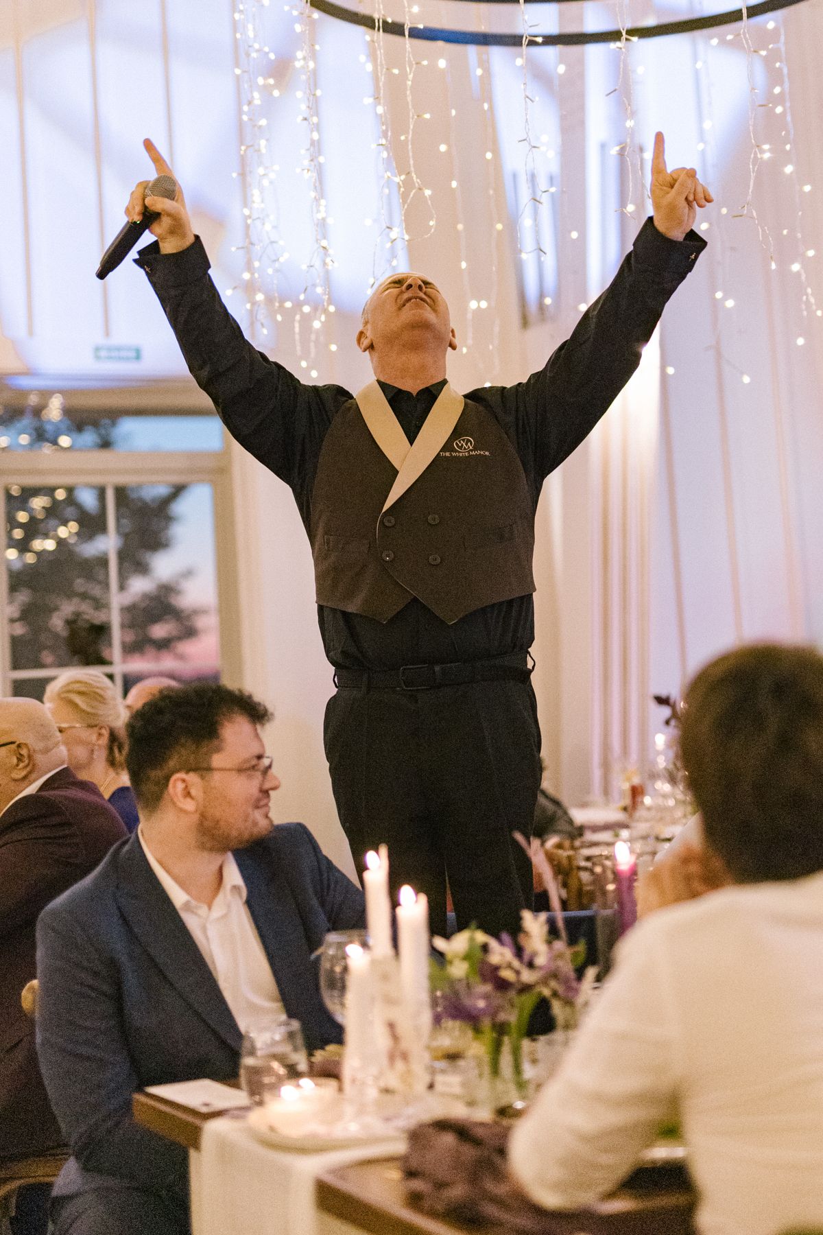 Wedding guests celebrating with arms raised during a festive reception dinner.