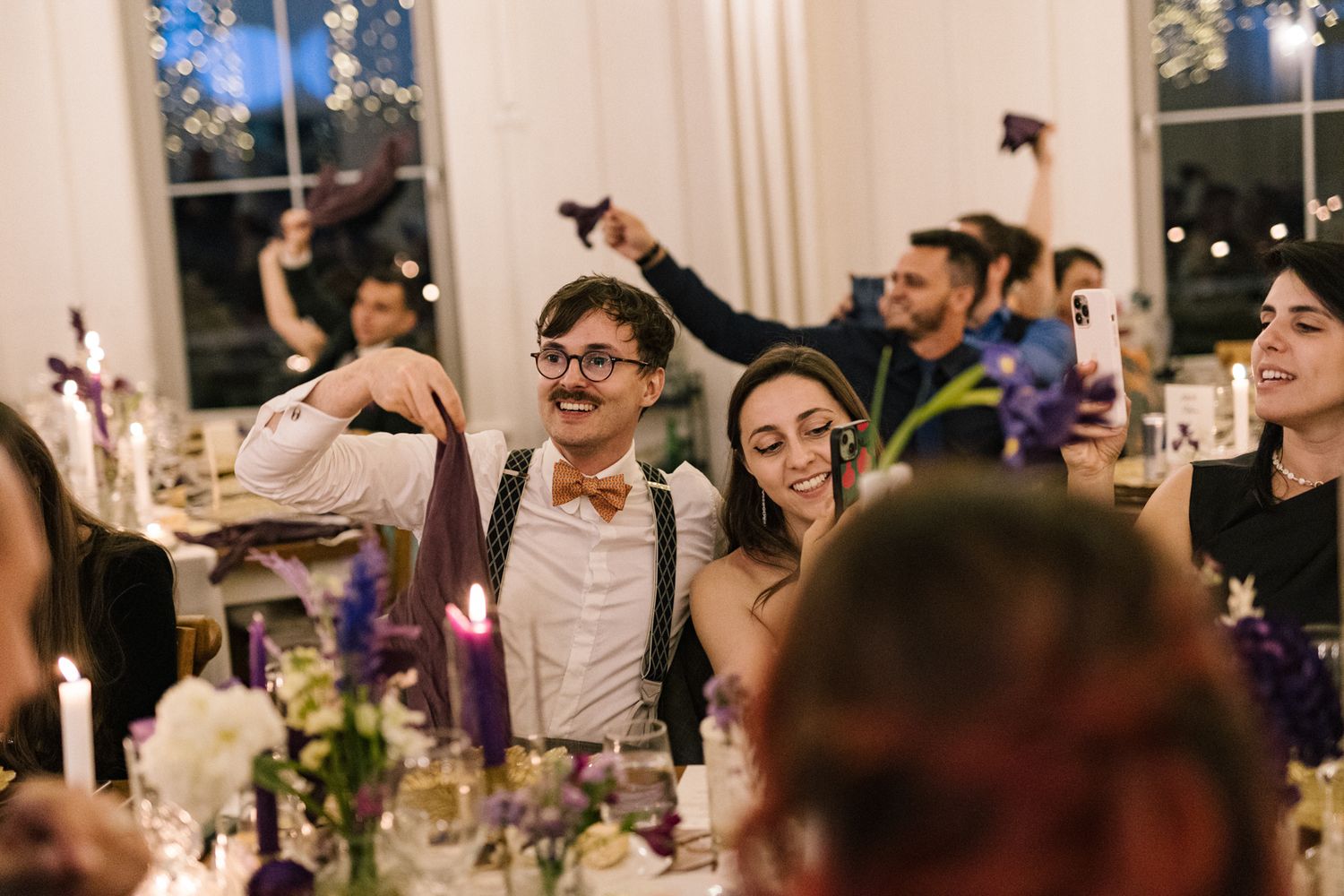 Wedding reception guests celebrating with animated expressions and raised hands.