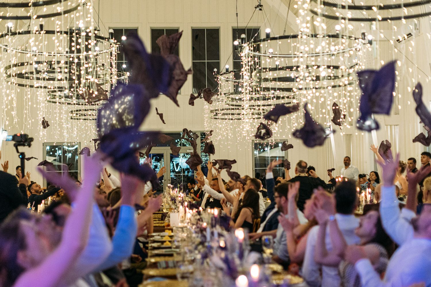Wedding reception venue decorated with string lights and filled with celebrating guests.
