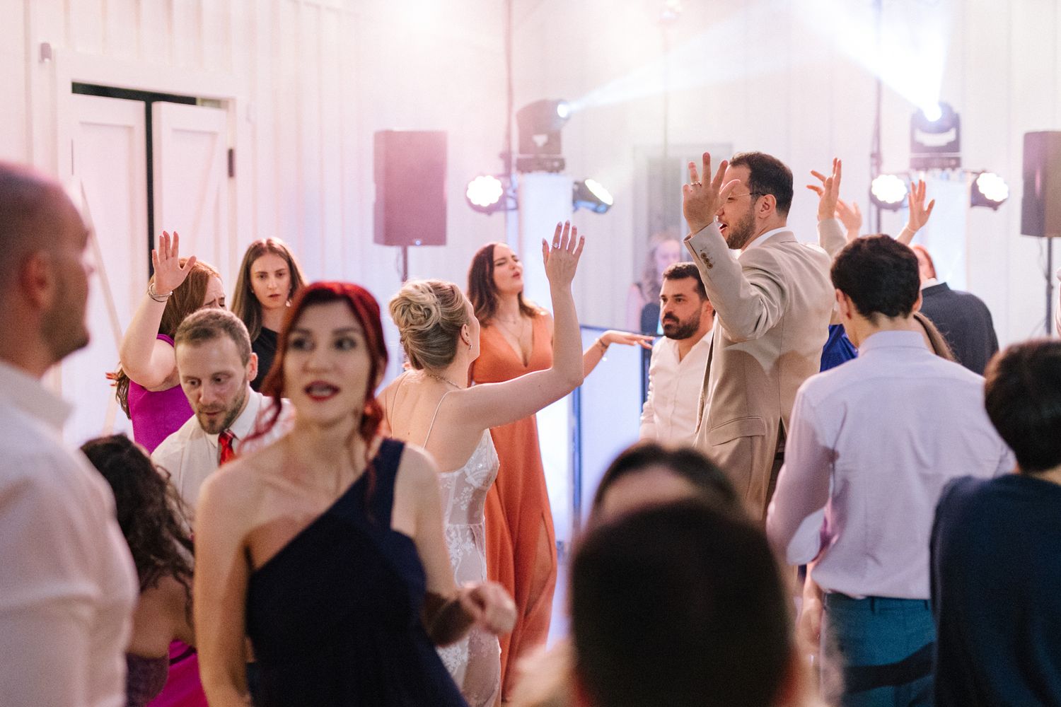 Energetic crowd dancing and celebrating at a lively indoor party with pink lighting.