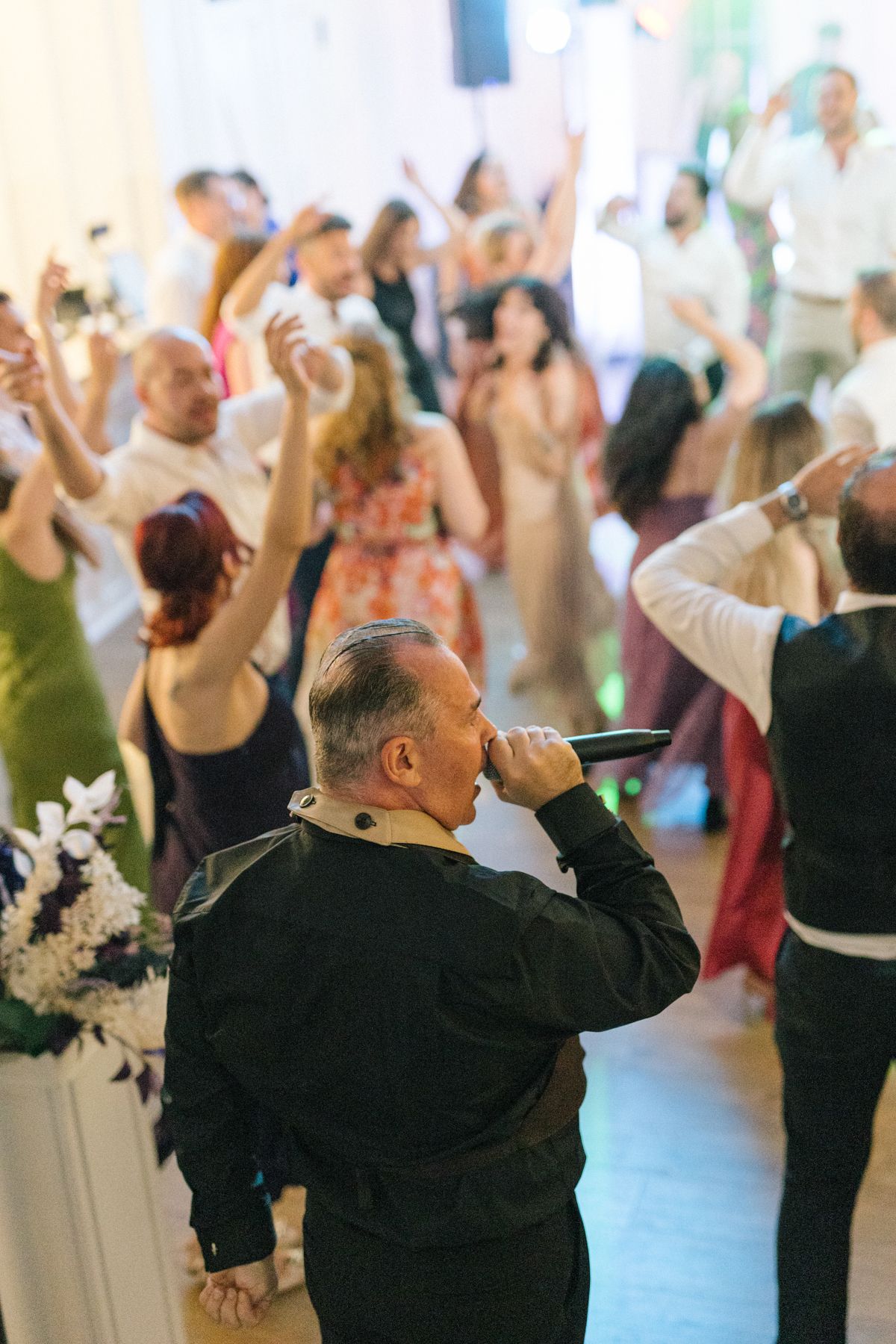 DJ performing at a crowded dance party with guests raising their hands in celebration.