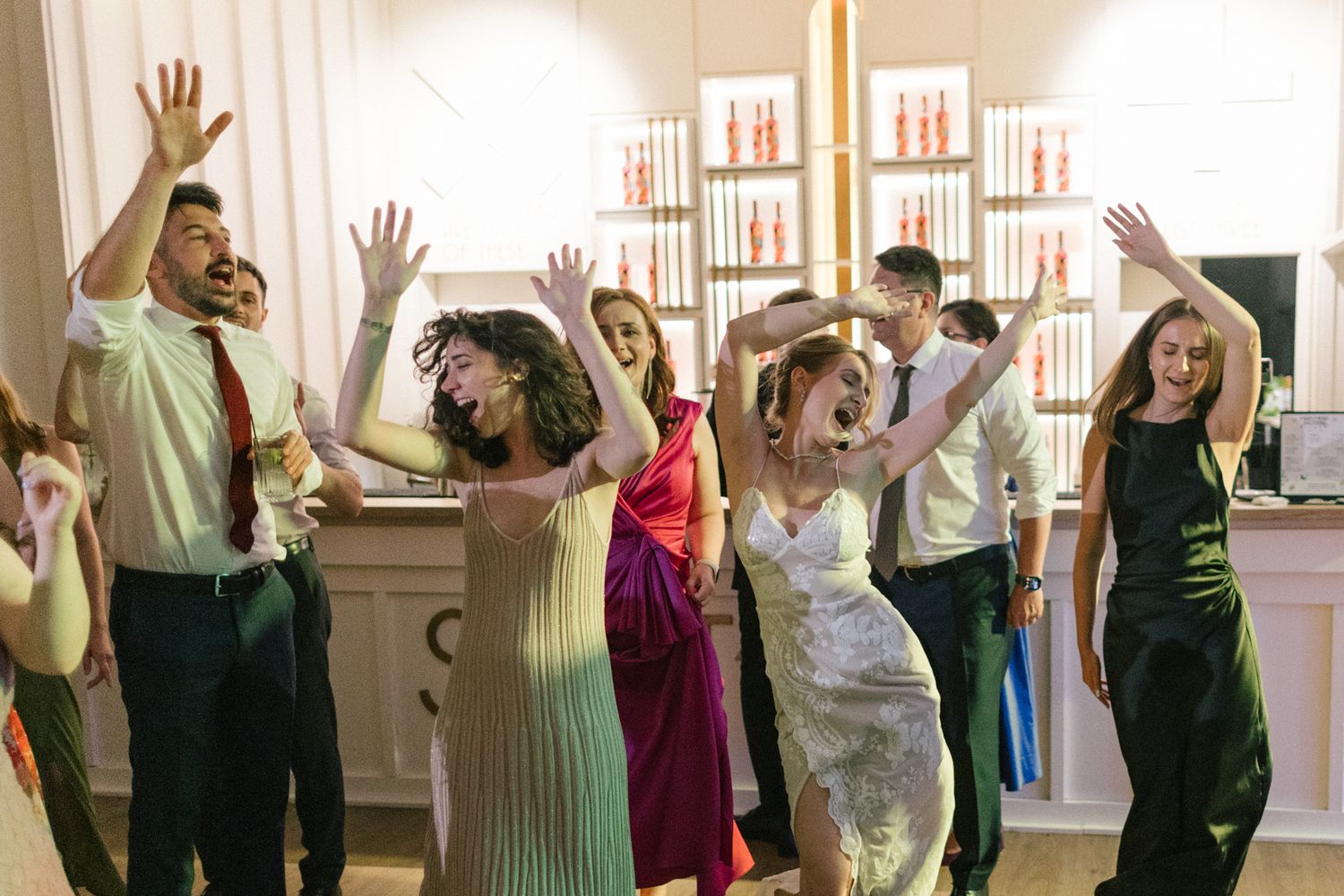 Group of party guests dancing with raised arms in front of an elegant fireplace display.