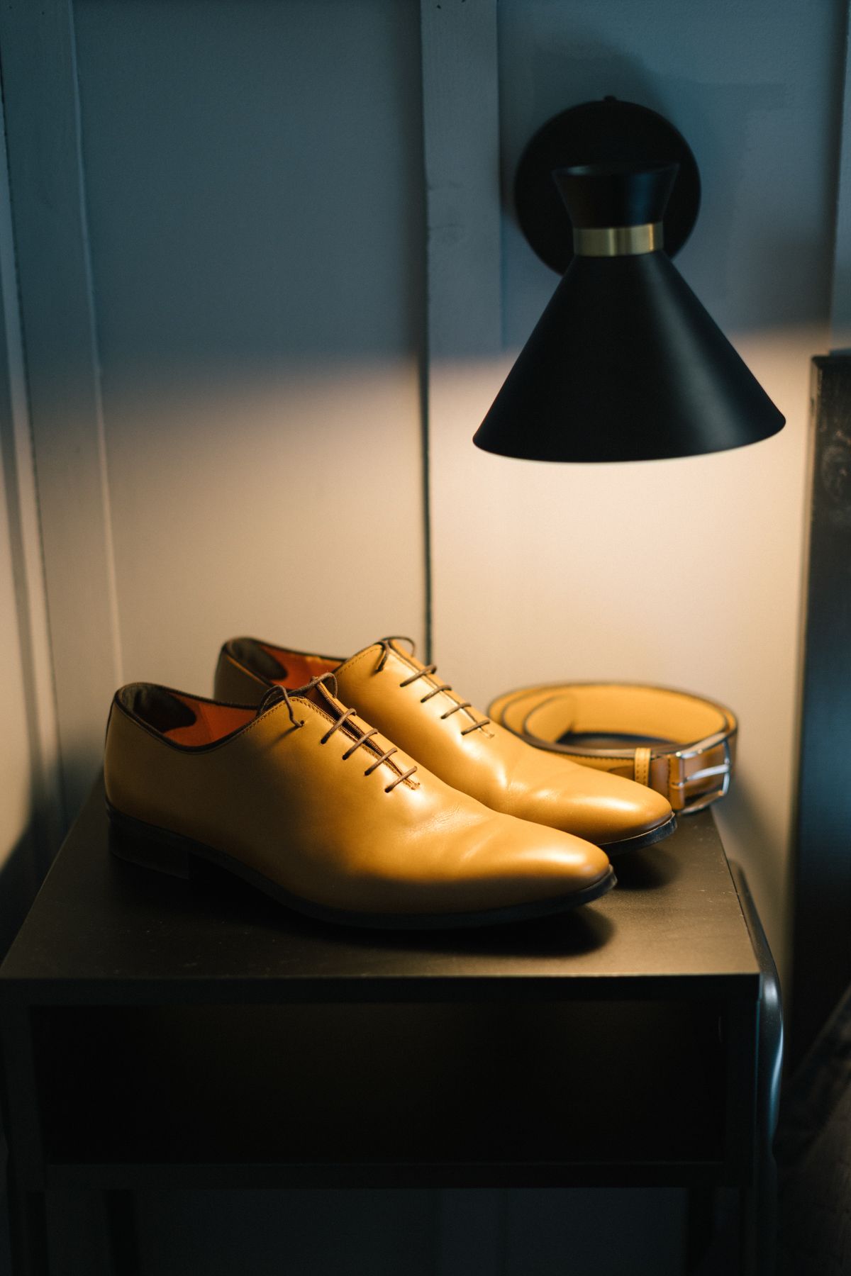Tan leather dress shoes displayed under dramatic lighting on a dark shelf.