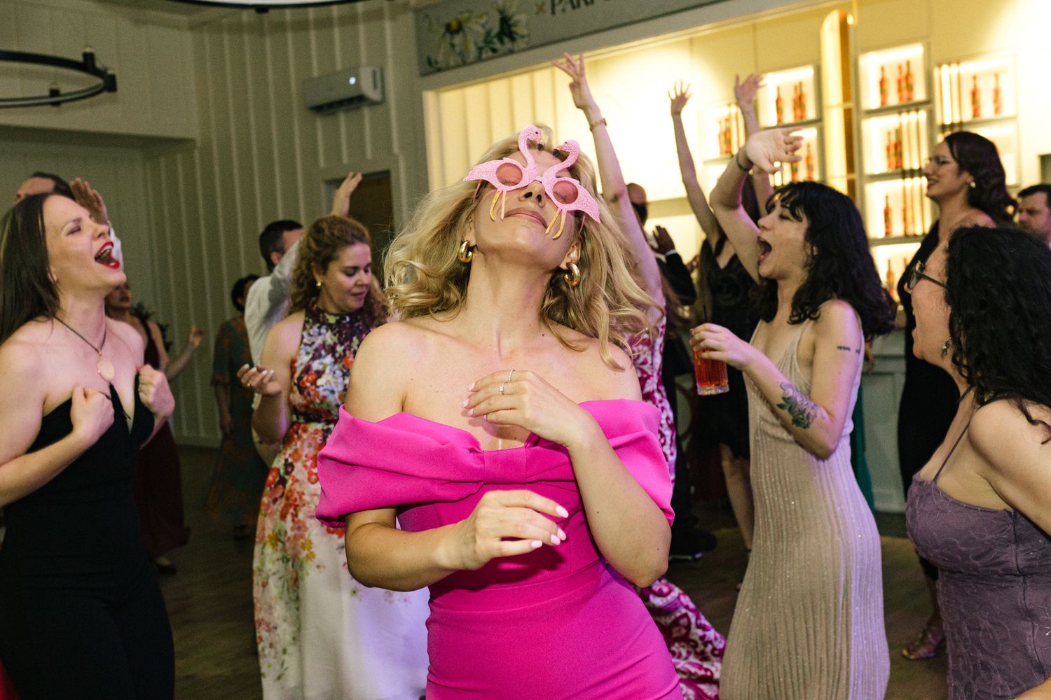 Party guests dancing and celebrating with raised arms at an indoor celebration.