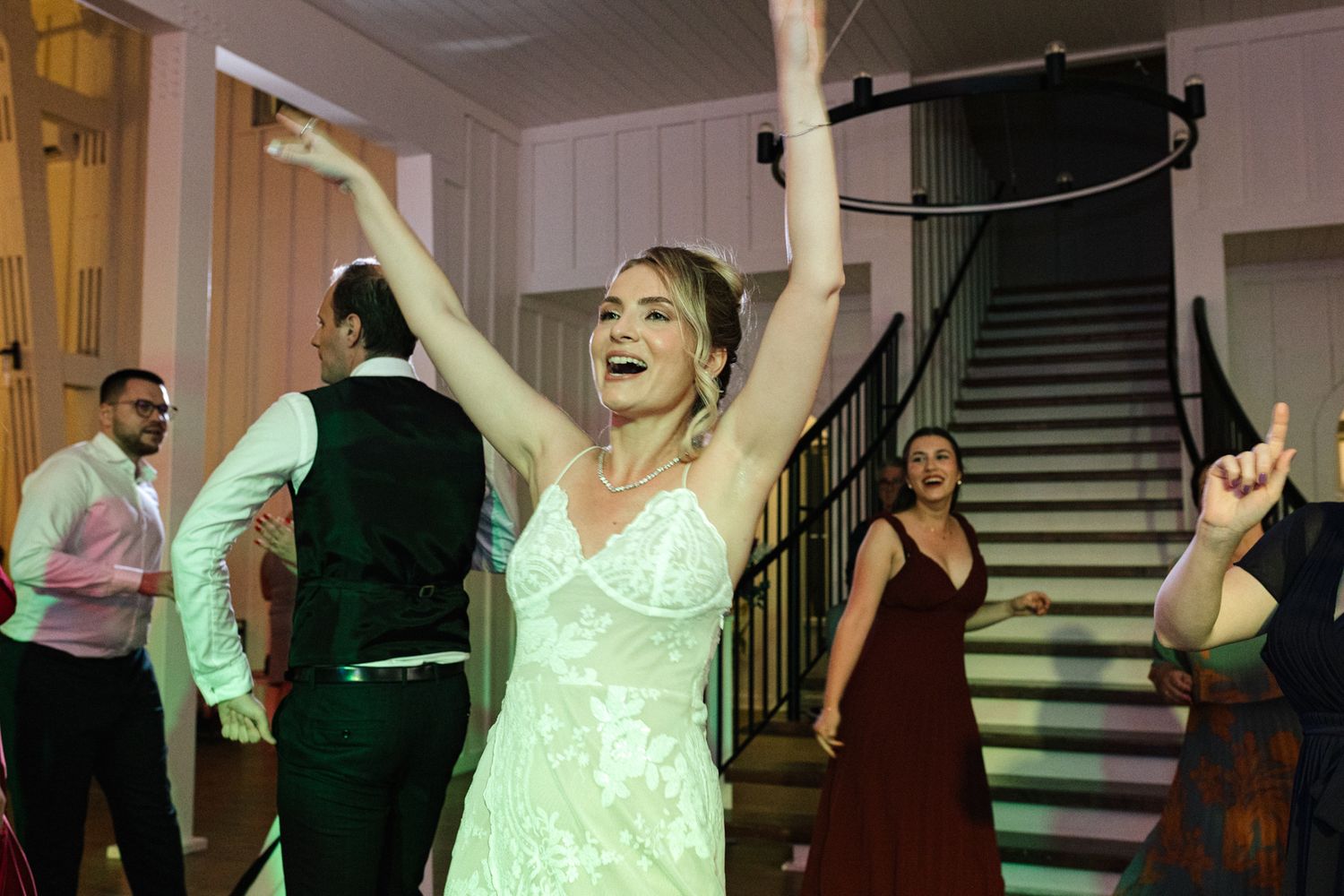 Guests dancing joyfully at a wedding reception with a bride in a white dress raising her arms in celebration.