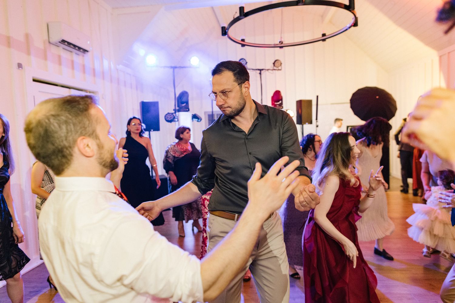 Wedding guests dancing and celebrating in a brightly lit indoor reception space.