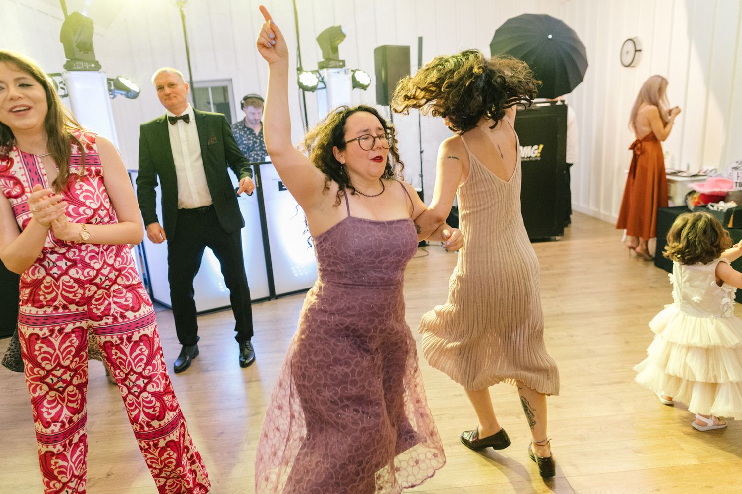 Wedding party dancing enthusiastically in colorful dresses at an indoor reception.