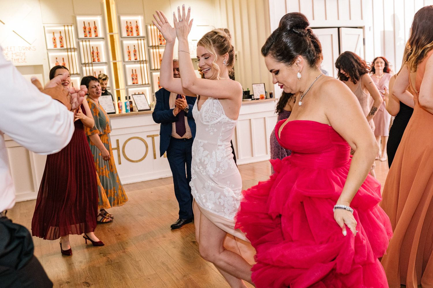 Wedding guests in formal attire dancing and celebrating on a wooden dance floor.