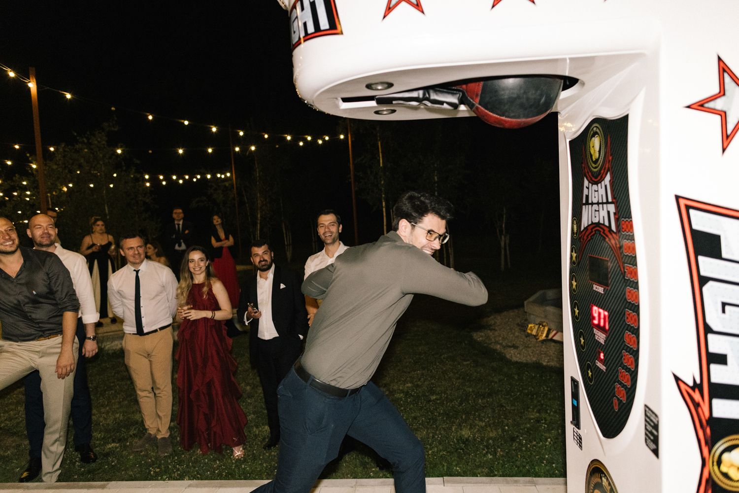 Guest showing off dance moves near an arcade game at an outdoor nighttime wedding reception.
