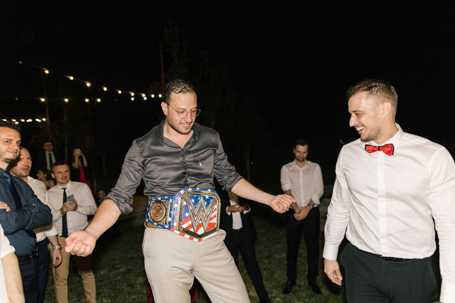 Wedding guests dancing and celebrating outdoors under string lights at night.