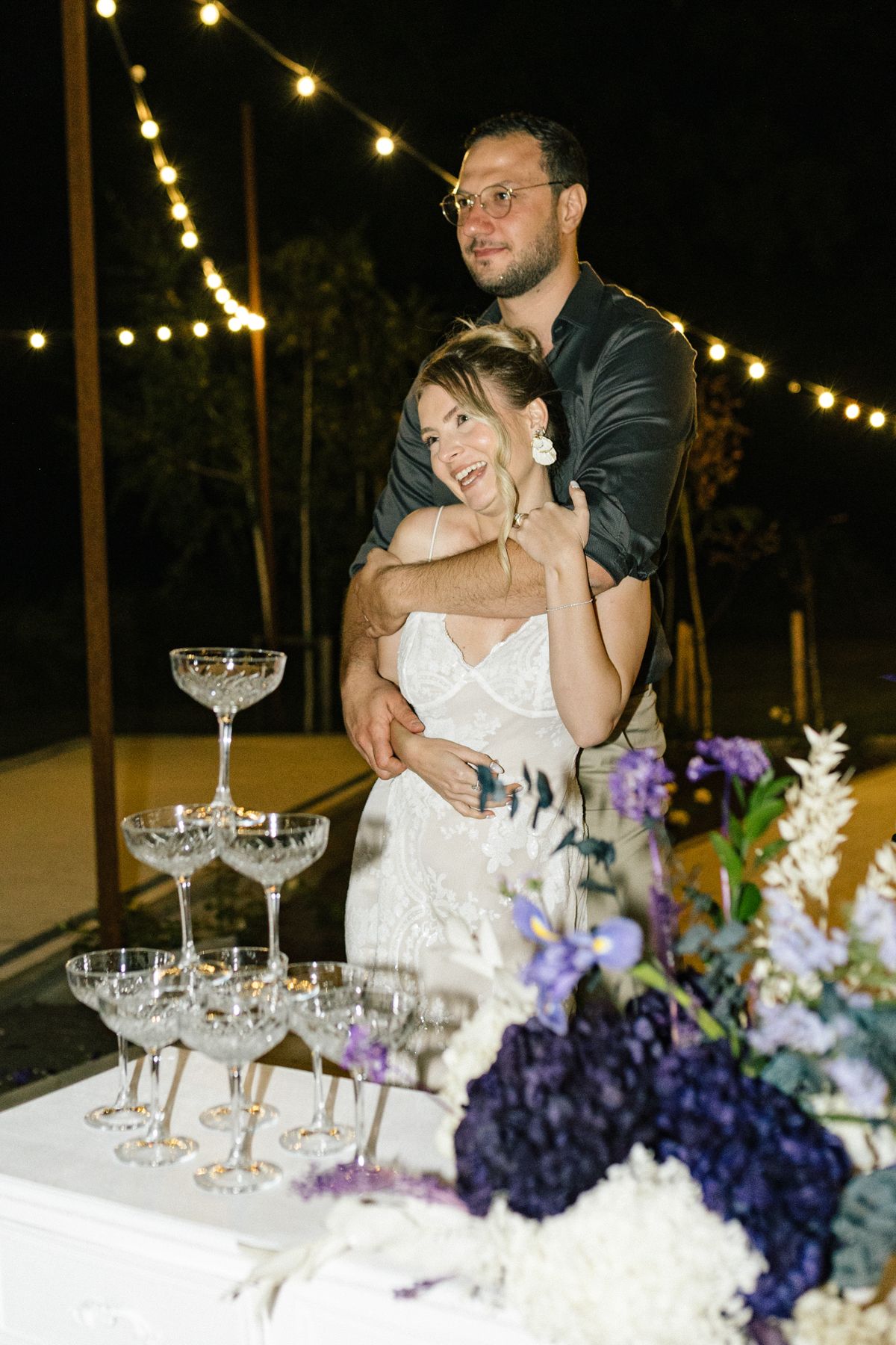 Romantic moment at wedding reception with champagne tower and purple floral decorations.