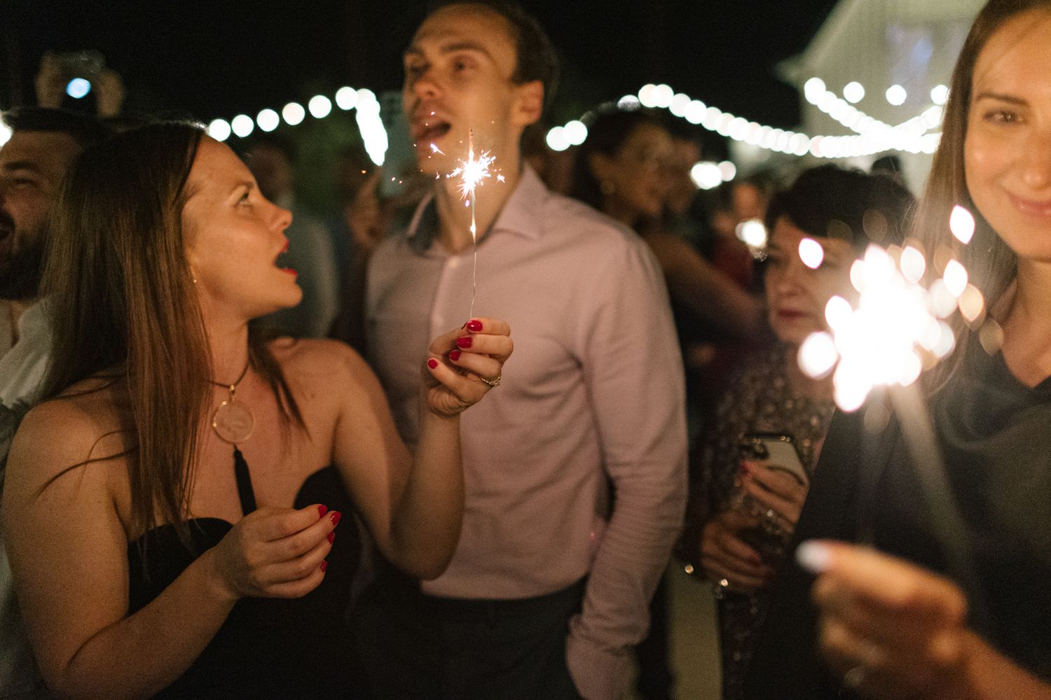 Wedding guests hold sparklers during an outdoor evening celebration.