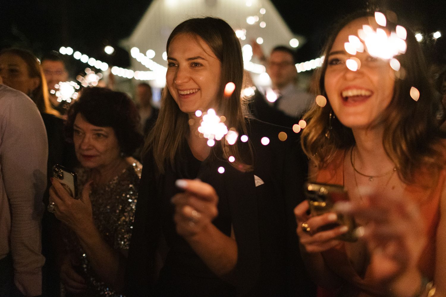 Nighttime celebration with guests holding sparklers under string lights.
