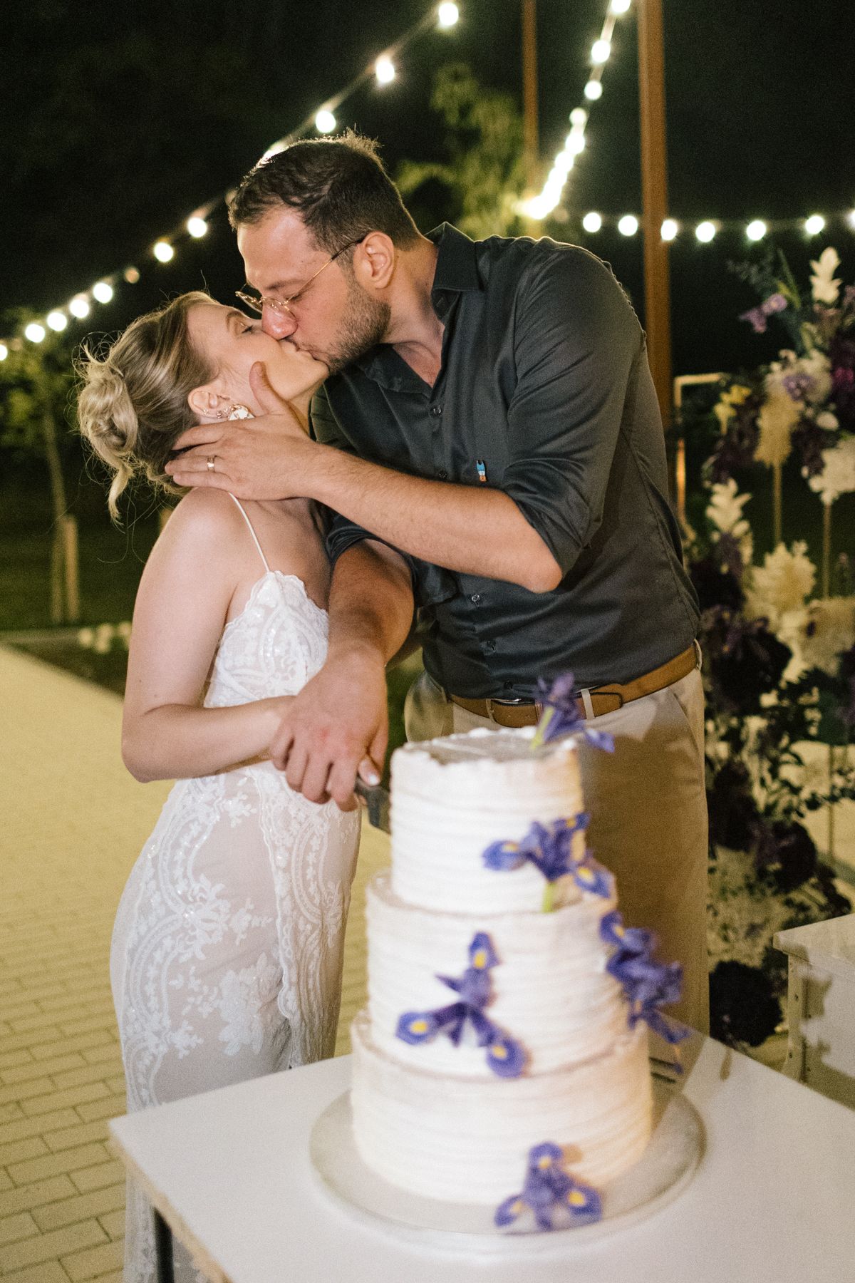 Newlyweds share a romantic moment beside their white and purple wedding cake.